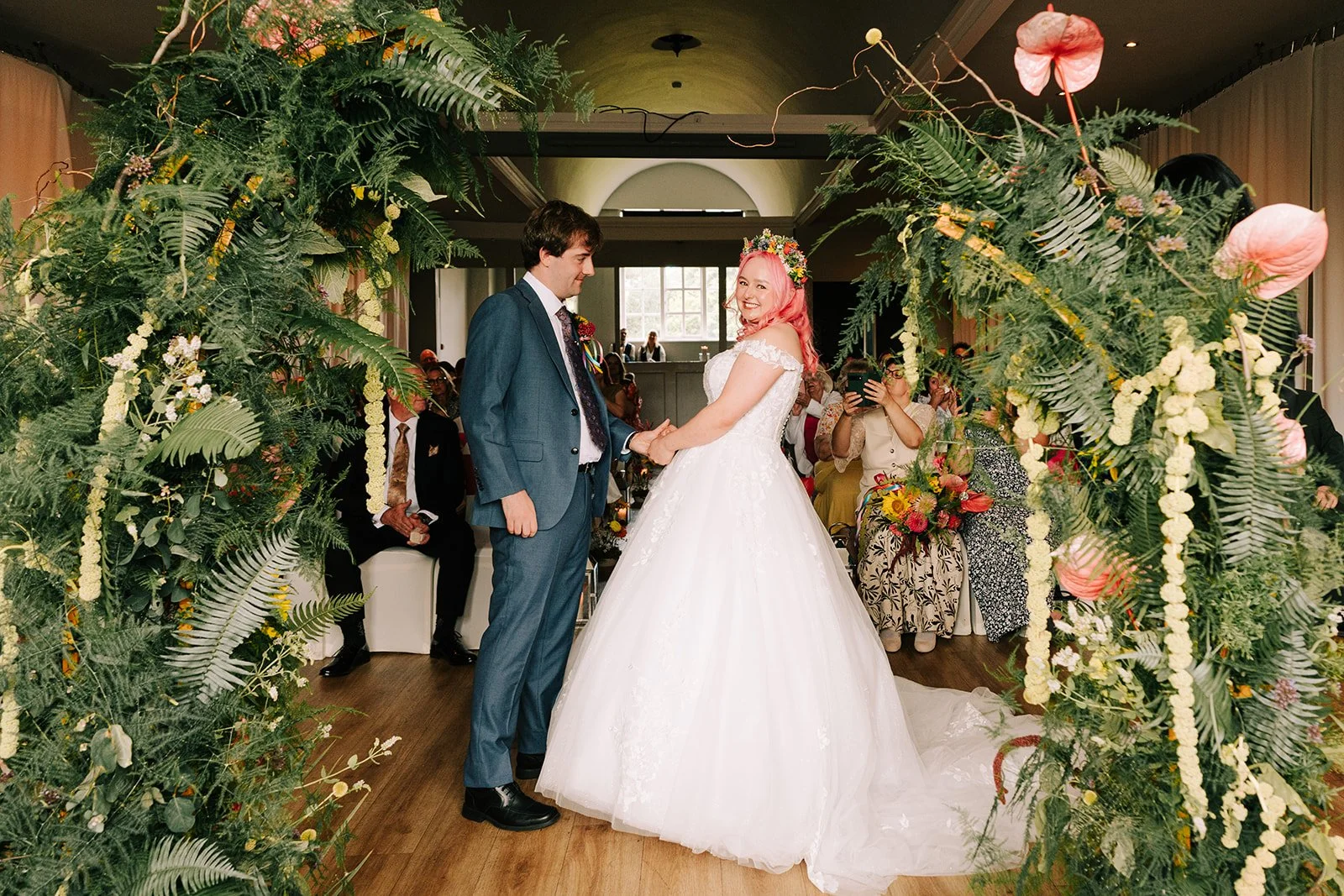 Colourful wedding couple behind colourful split arch created by MillieBuds Colour Loving Wedding Florist in Stockport at Bowdon Rooms