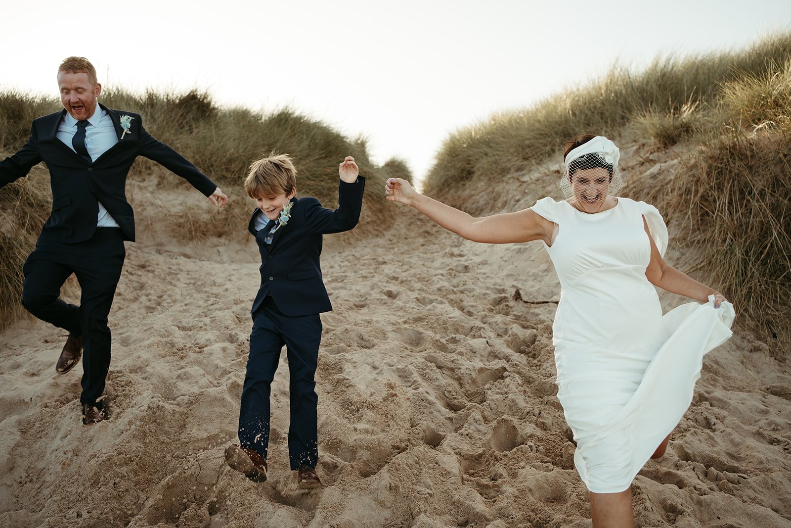 Family running down sand dunes at coastal wedding