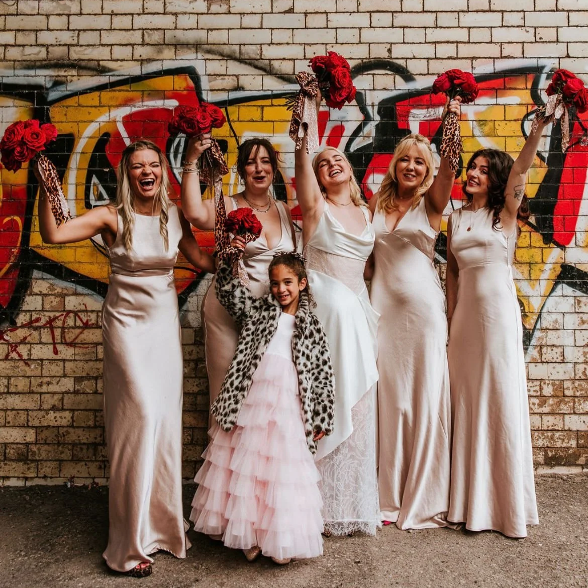 Bridal party in front of graffiti sign with red rose bouquets and leopard print bows