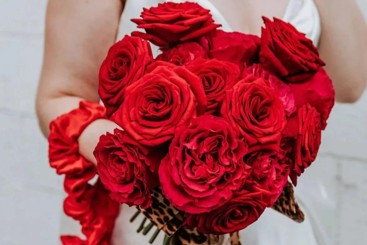 A person holding a bouquet of red roses with a leopard print wrapping.