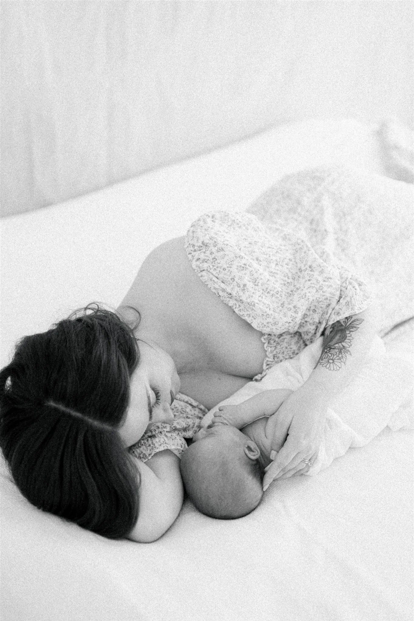 A woman lying on her side in bed, cuddling a newborn baby.