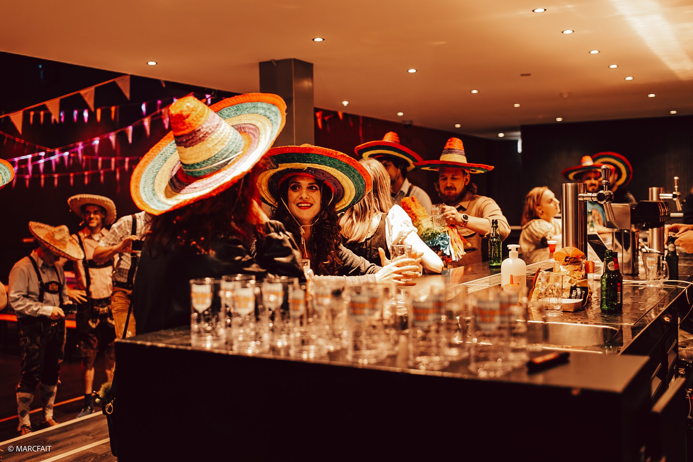 People at a bar wearing colorful sombreros celebrating a festive event, with drinks and decorations.