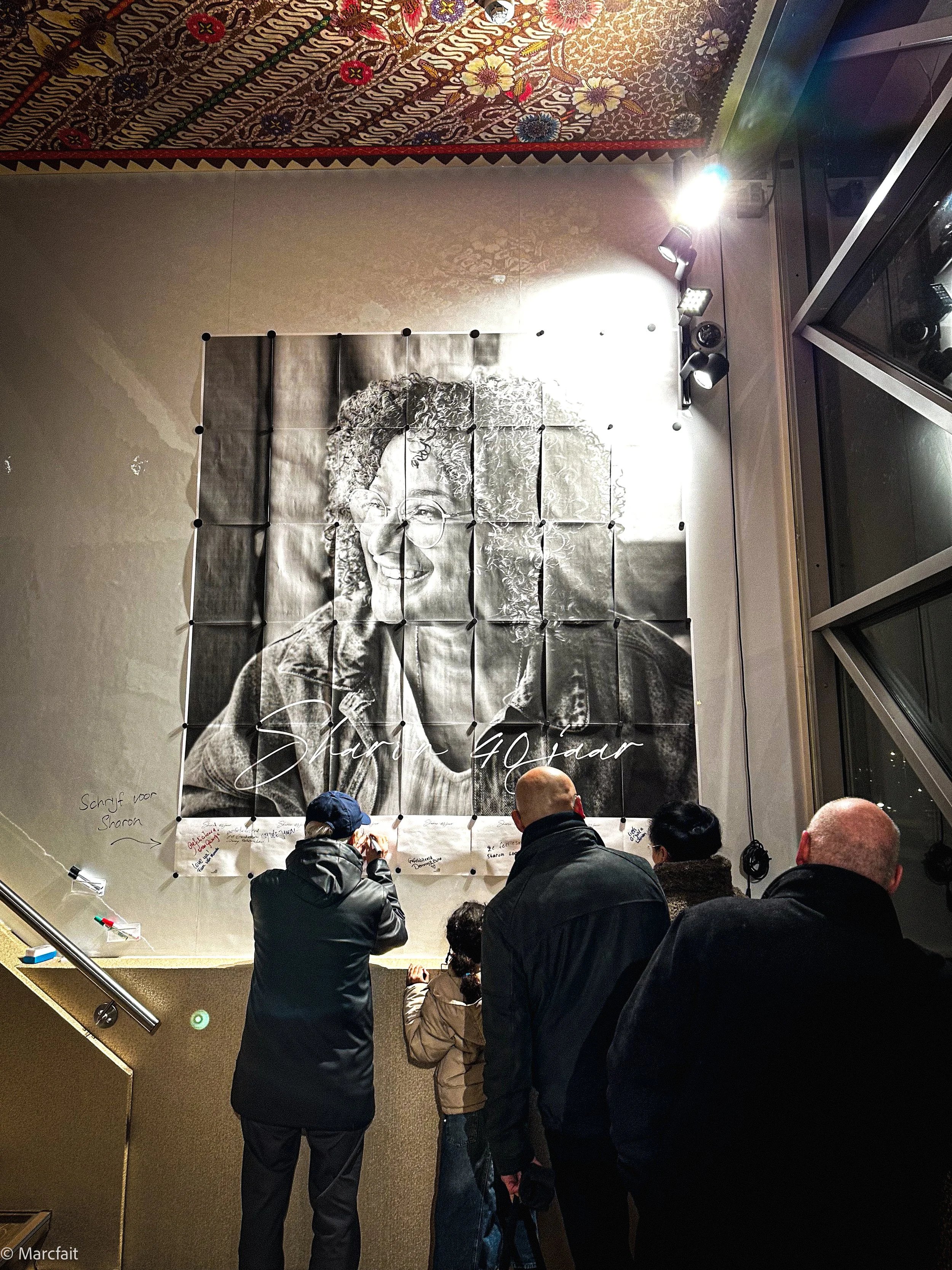 A large birthday card was displayed on the MARCFAIT magnetic wall. Several people are gathered in front of it, signing and writing their best wishes.