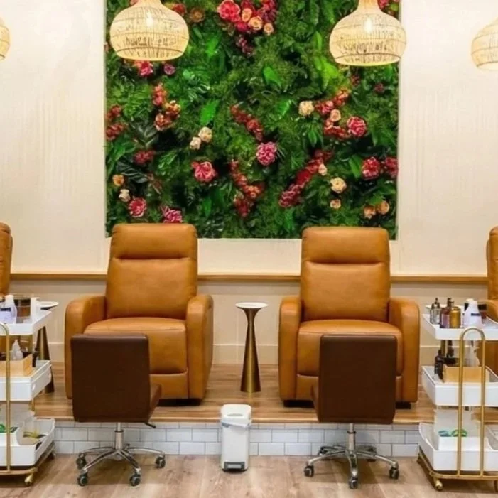 Boutique nail spa's pedicure station featuring reclining leather chairs chairs. The background features a floral green wall with pink flowers.