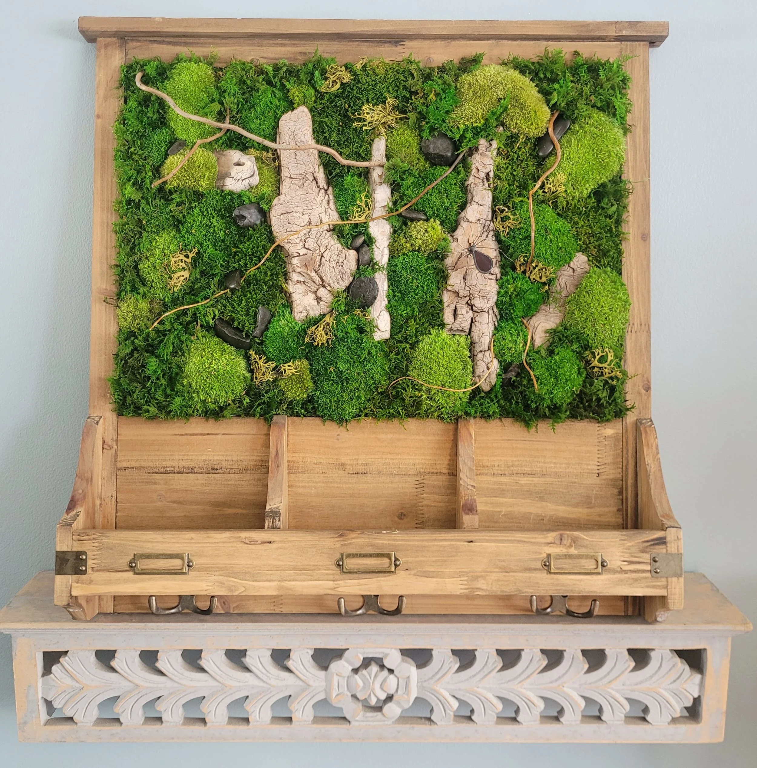 Wooden wall shelf with mounted green moss, stones, and bark art piece, on a carved wooden bracket.