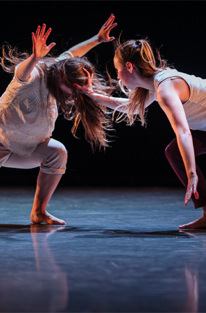 two female dancers, one with arms out, while the other has their hand on the other's head