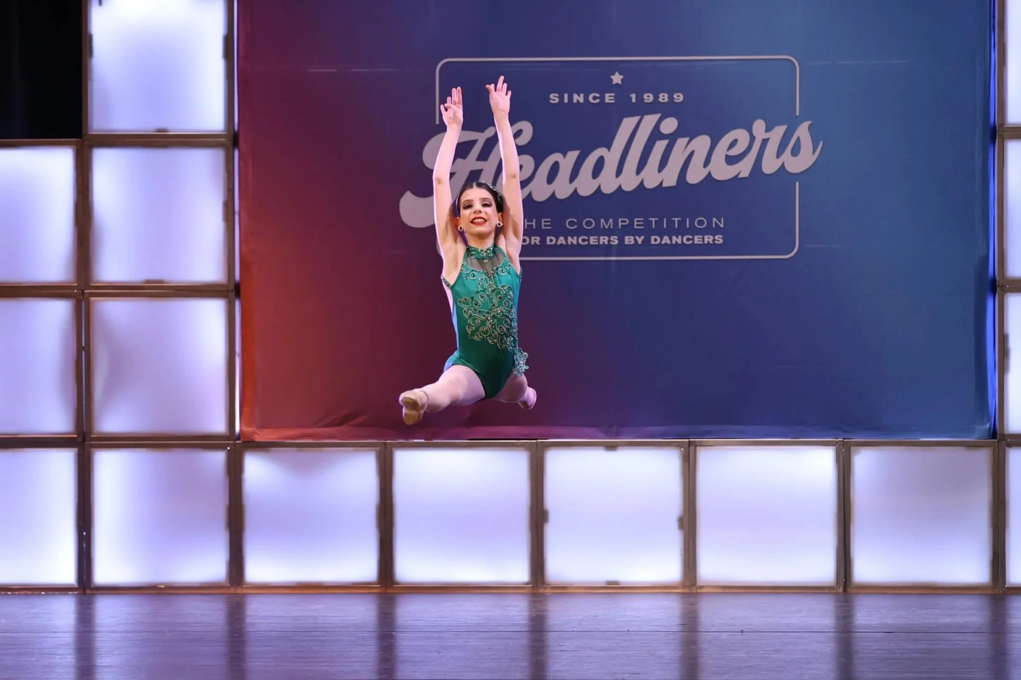 A young girl performing a dance leap on stage during a dance competition.