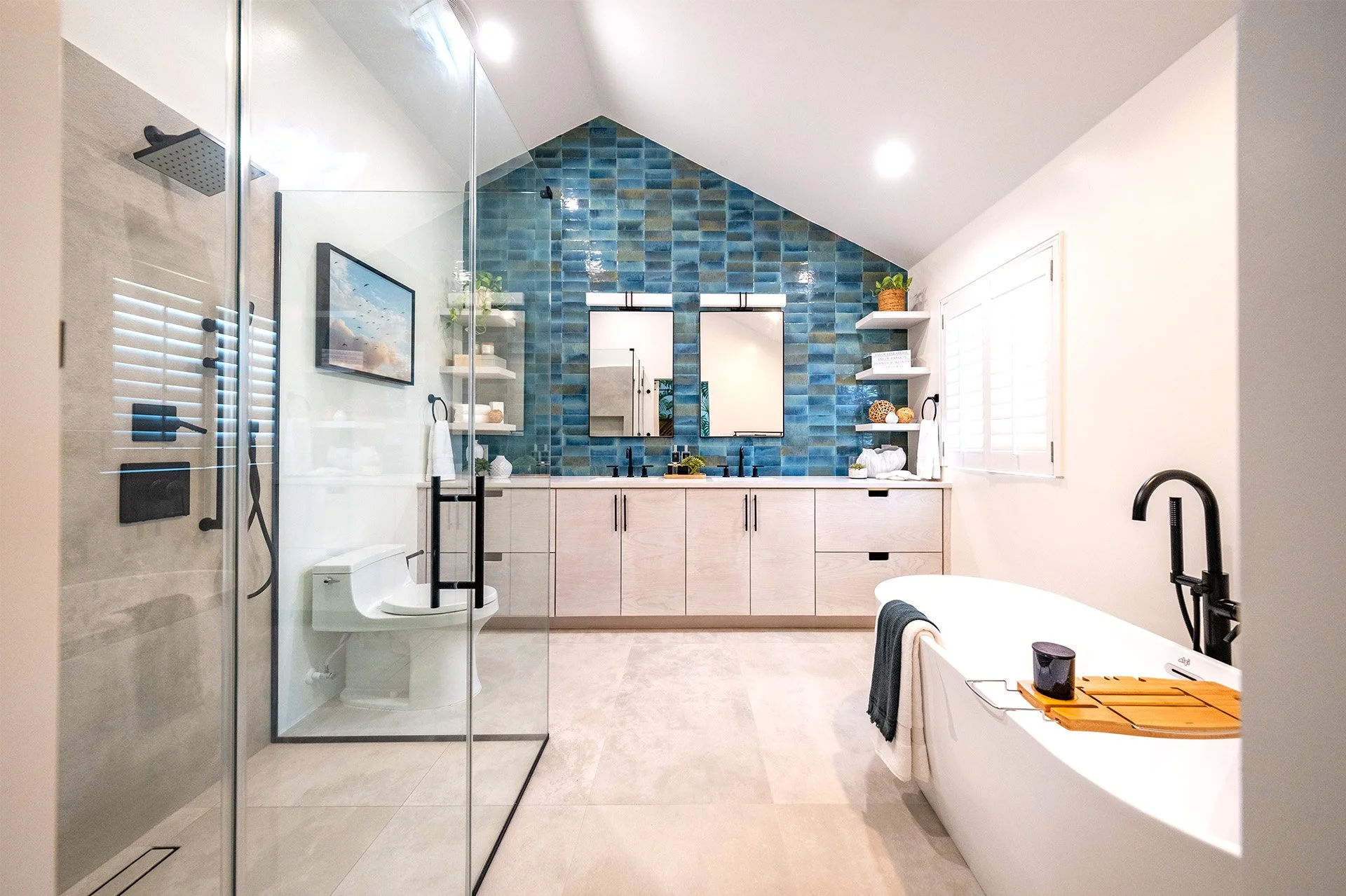 Modern bathroom with glass shower, a freestanding bathtub, a dual sink vanity with mirrors, and colorful blue tile accent wall.