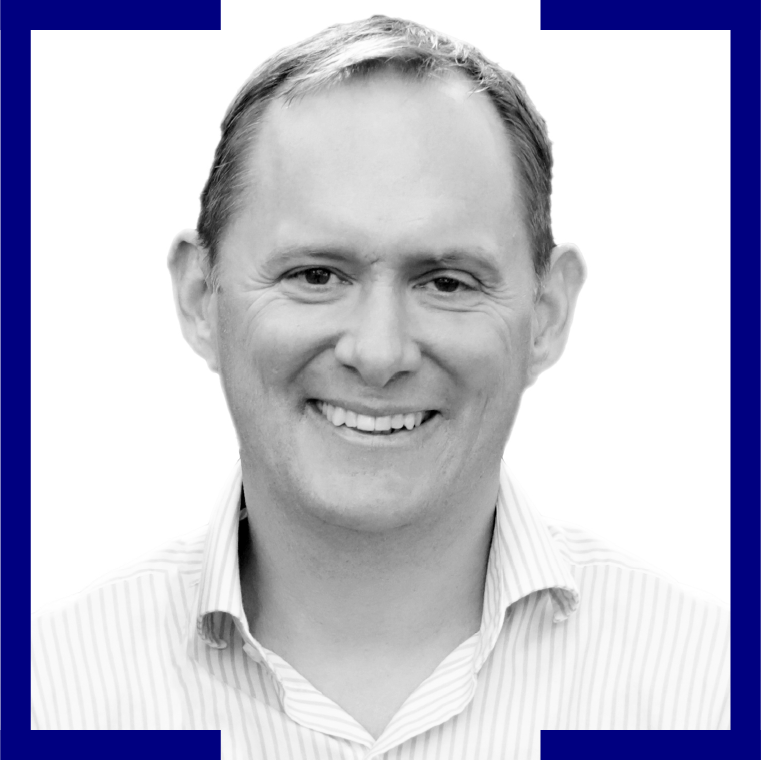 Black and white portrait of a smiling man with short hair, wearing a striped collared shirt, framed by a blue border.