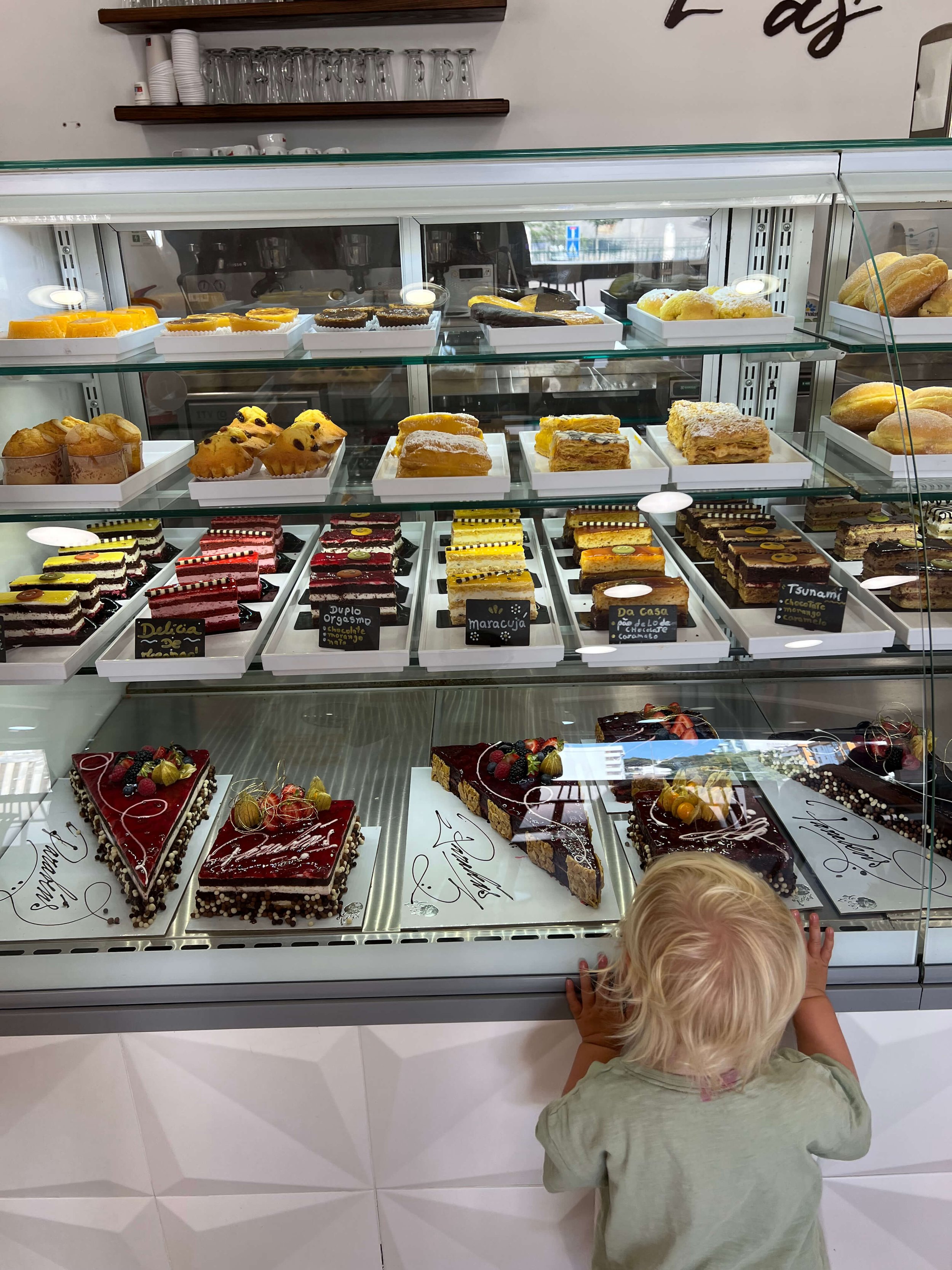 Child looking at the pastry display case full of cakes at Delicias bakery Lagos