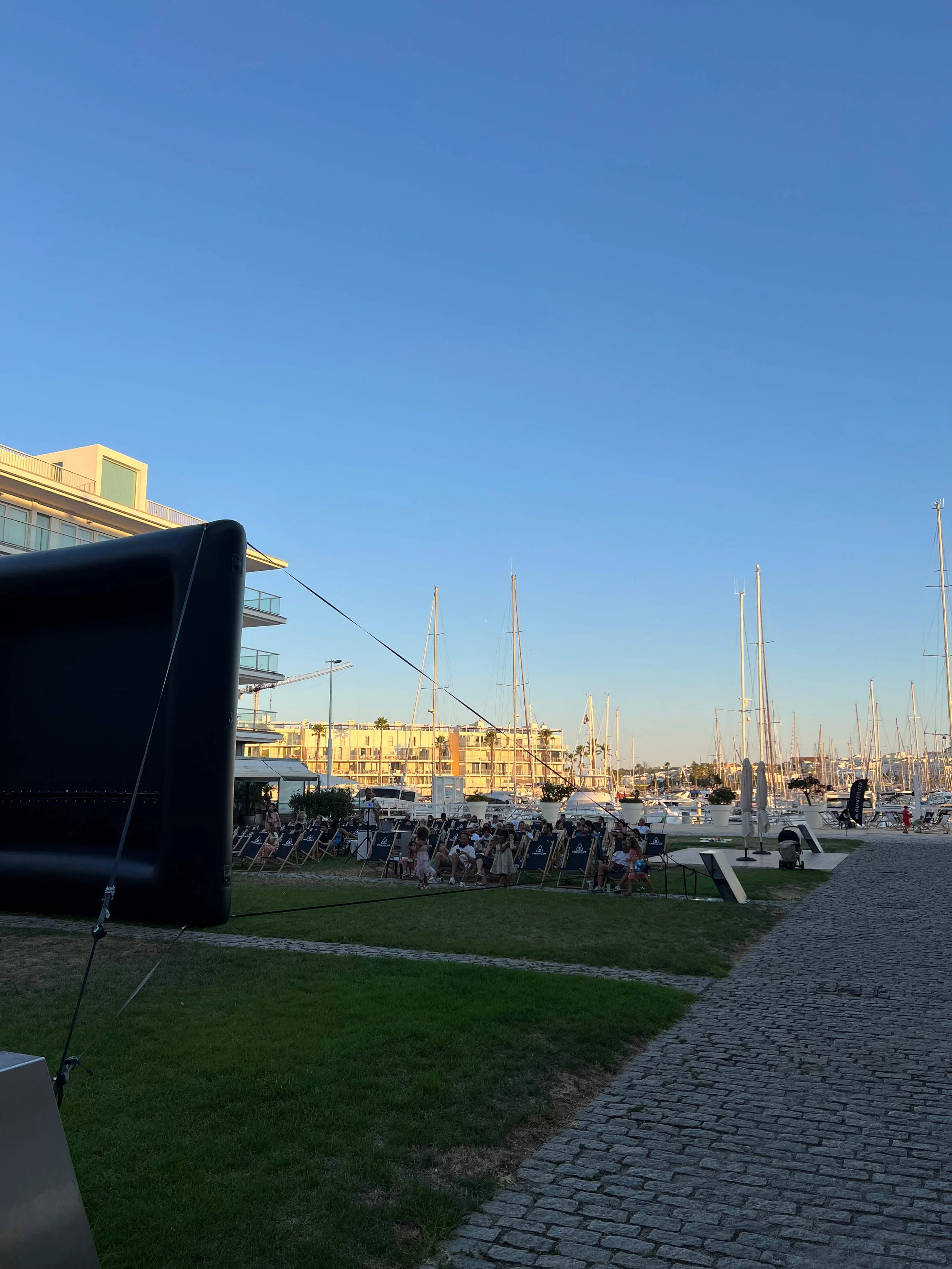 Inflatable cinema screen set up on the lawn at Lagos marina with deckchairs facing the boats at golden hour