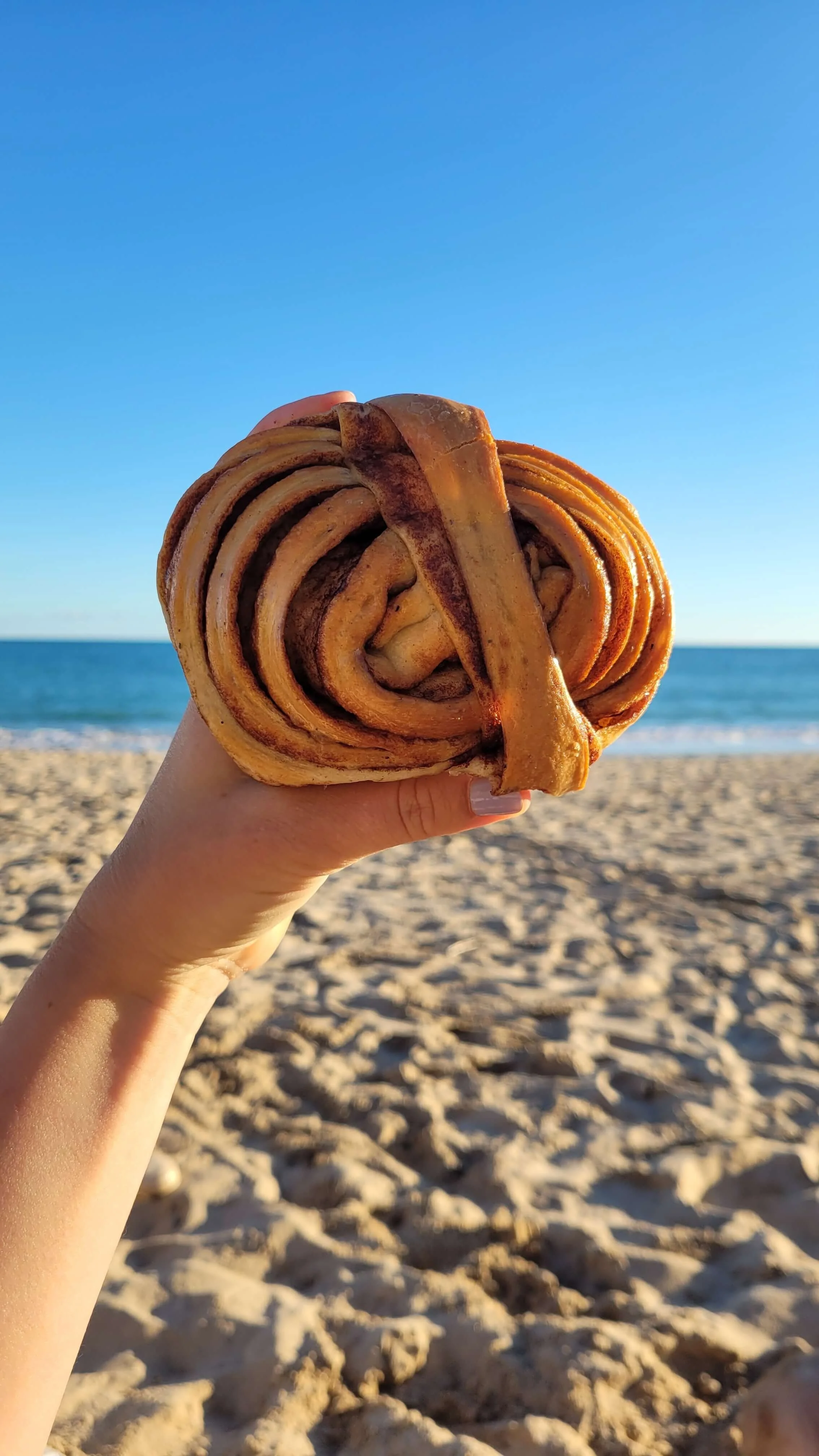 Holding a cinnamon bun from All Things Dough on the beach in Lagos Algarve