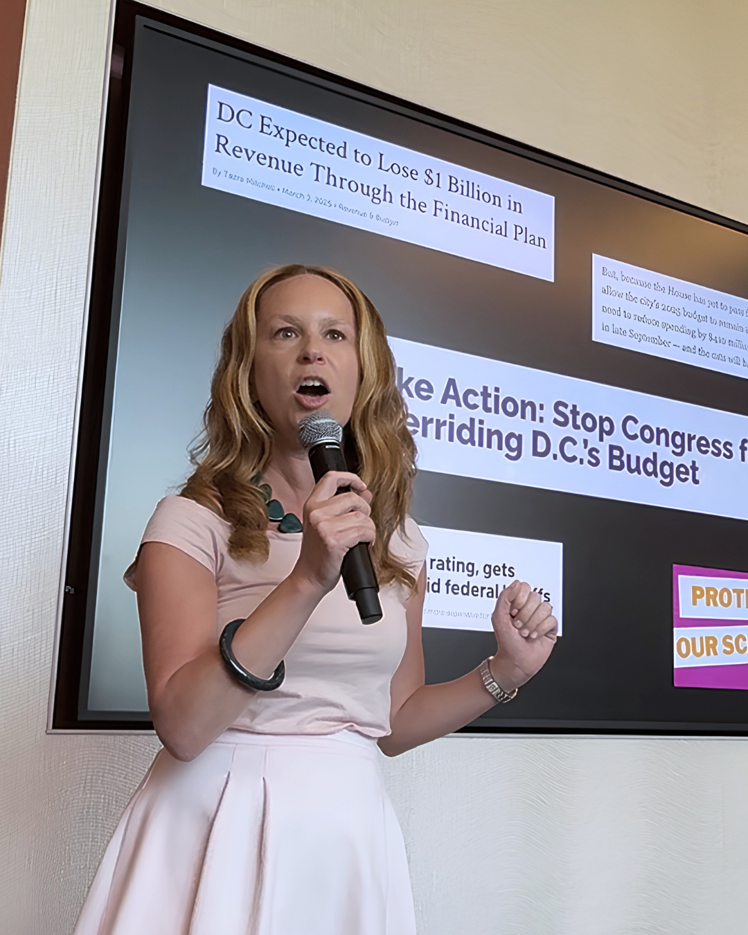Rebecca Ballard holding a microphone and speaking in front of a presentation slide about the D.C. financial plan and budget.