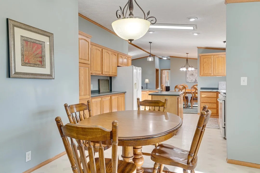 View of a kitchen and dining area with light wood cabinets, a white refrigerator, and a round wooden table with four chairs.