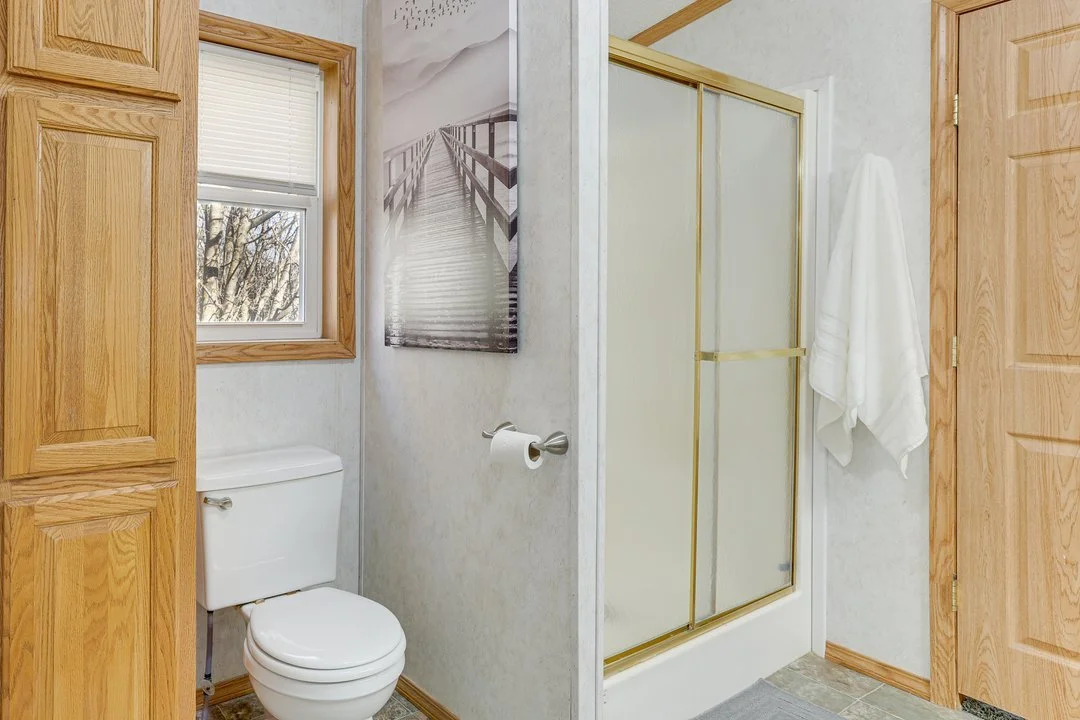 Bathroom with a toilet next to a window and a shower with frosted glass doors.