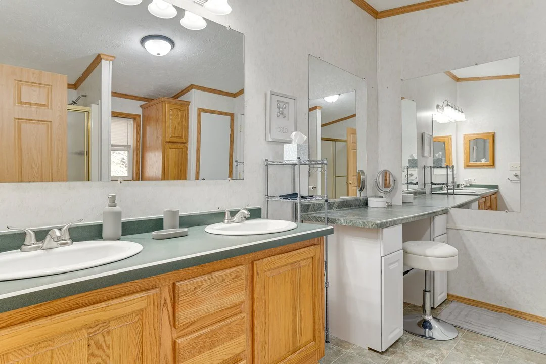 Bathroom with dual sinks, large mirrors, wooden cabinets, and a small seating area with a stool.