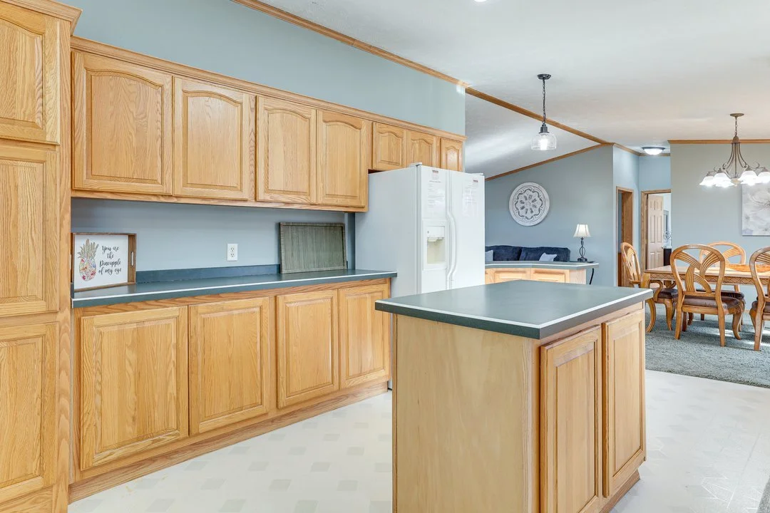 A kitchen with wooden cabinets, a white refrigerator, a small island, and a view of a dining area with a table and chairs.