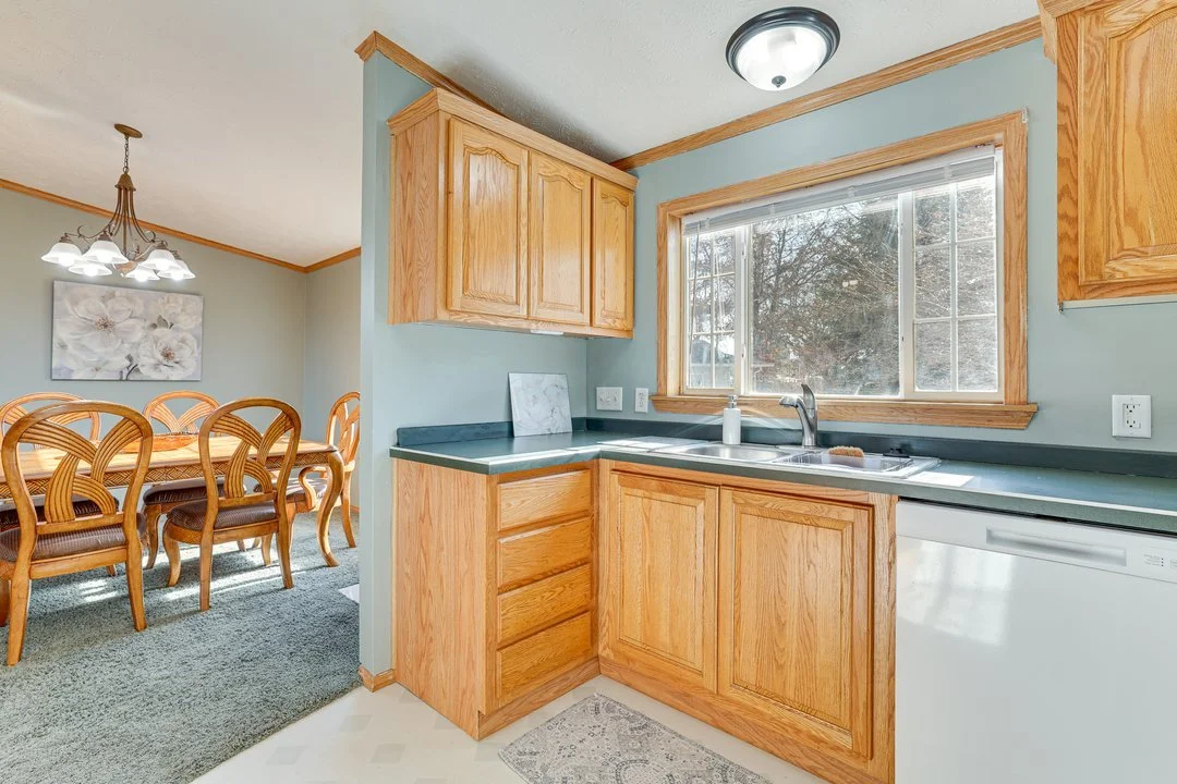 Kitchen with wooden cabinets, a window above the sink, and a view of a dining room with a wooden table and chairs.