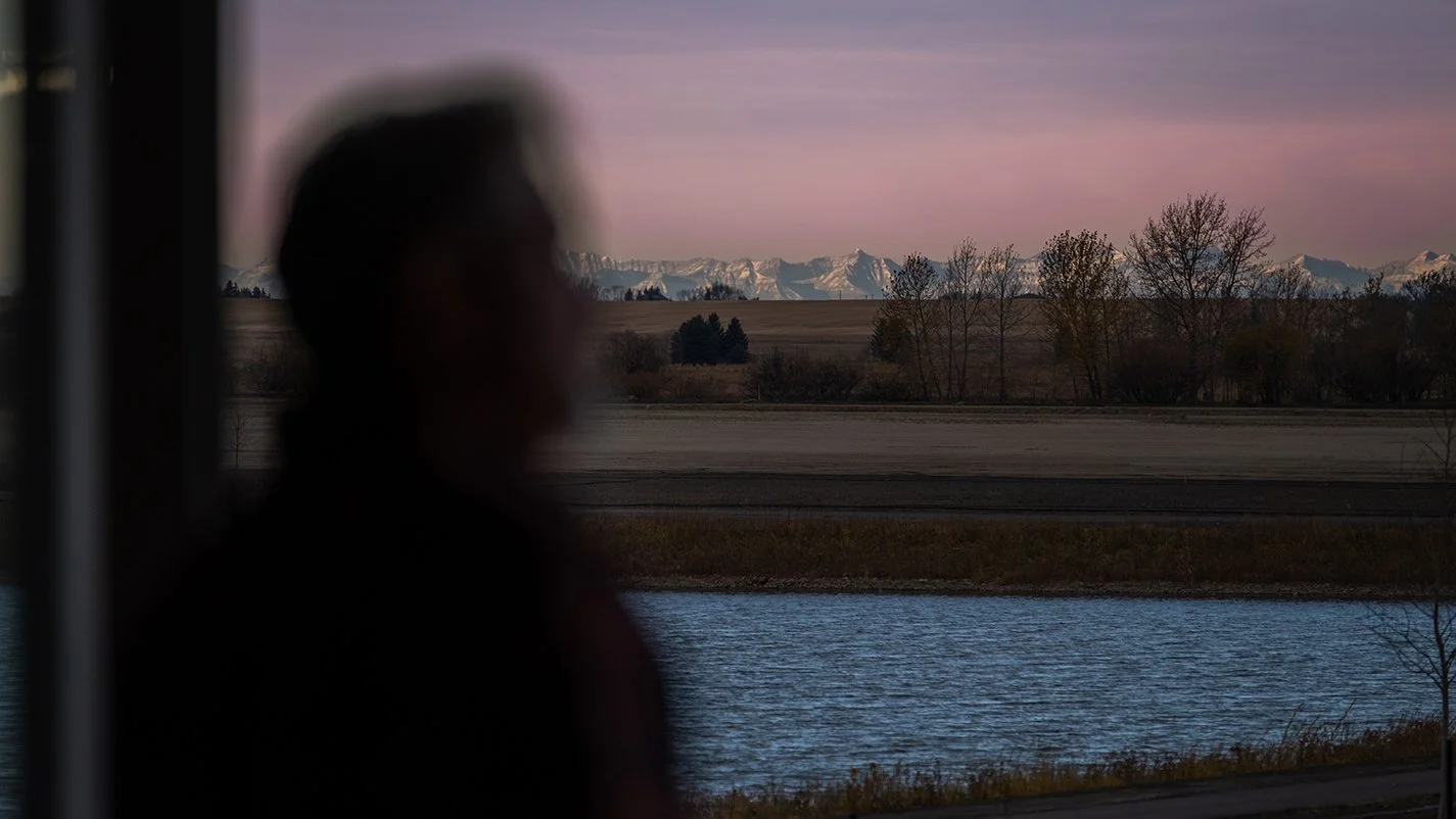 Image of the Rockies at dusk in the background, water in the foreground and the siloute of a person close to the camera