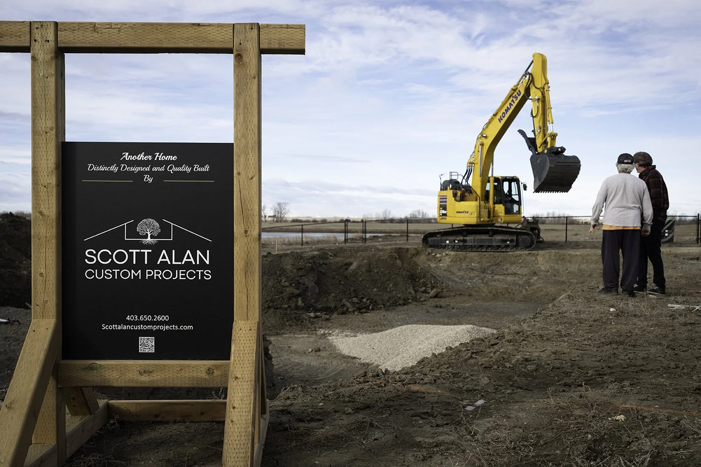 Image of empty lot with two people having a discussion, standing in front of a large back-hoe