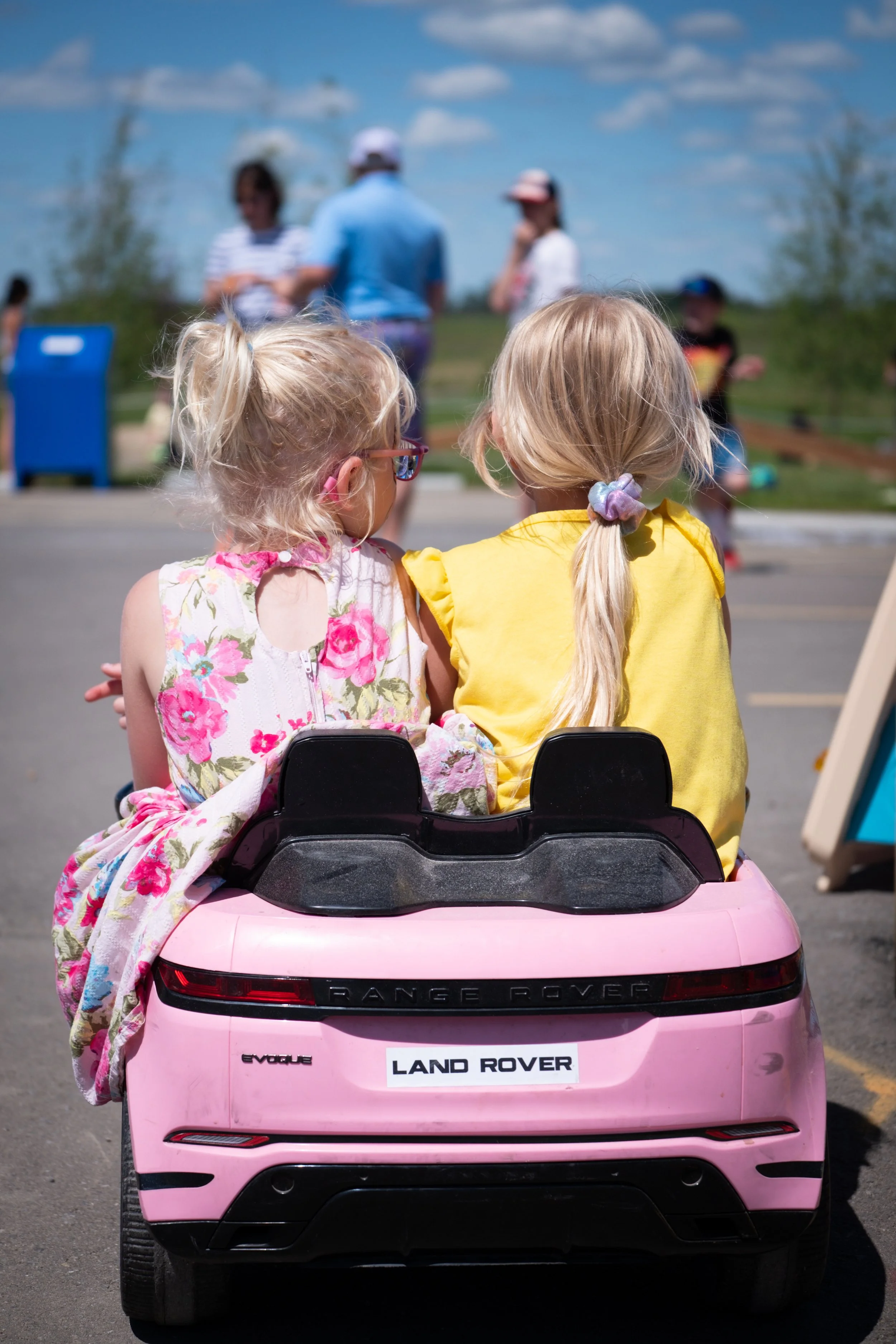 Image of two young girls sitting in a pink toy car
