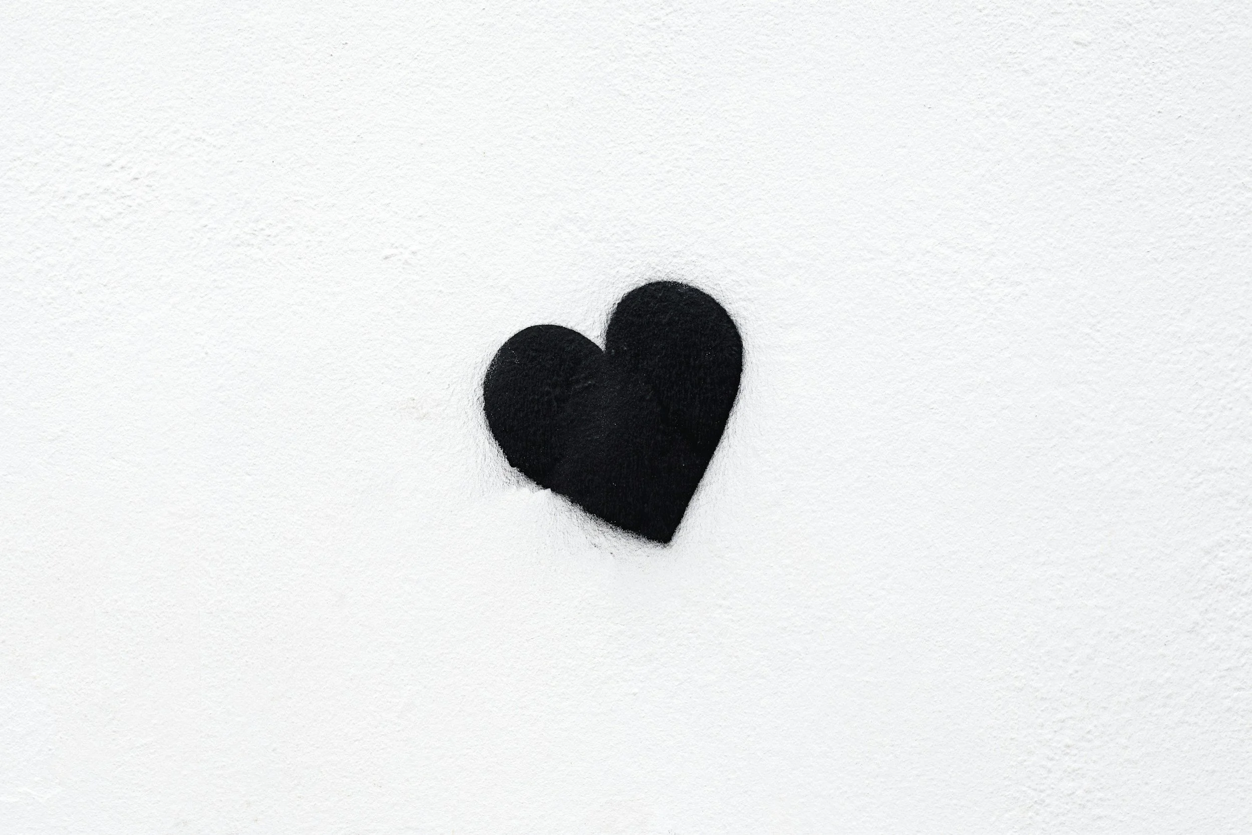 A black heart symbol painted on a white textured wall.