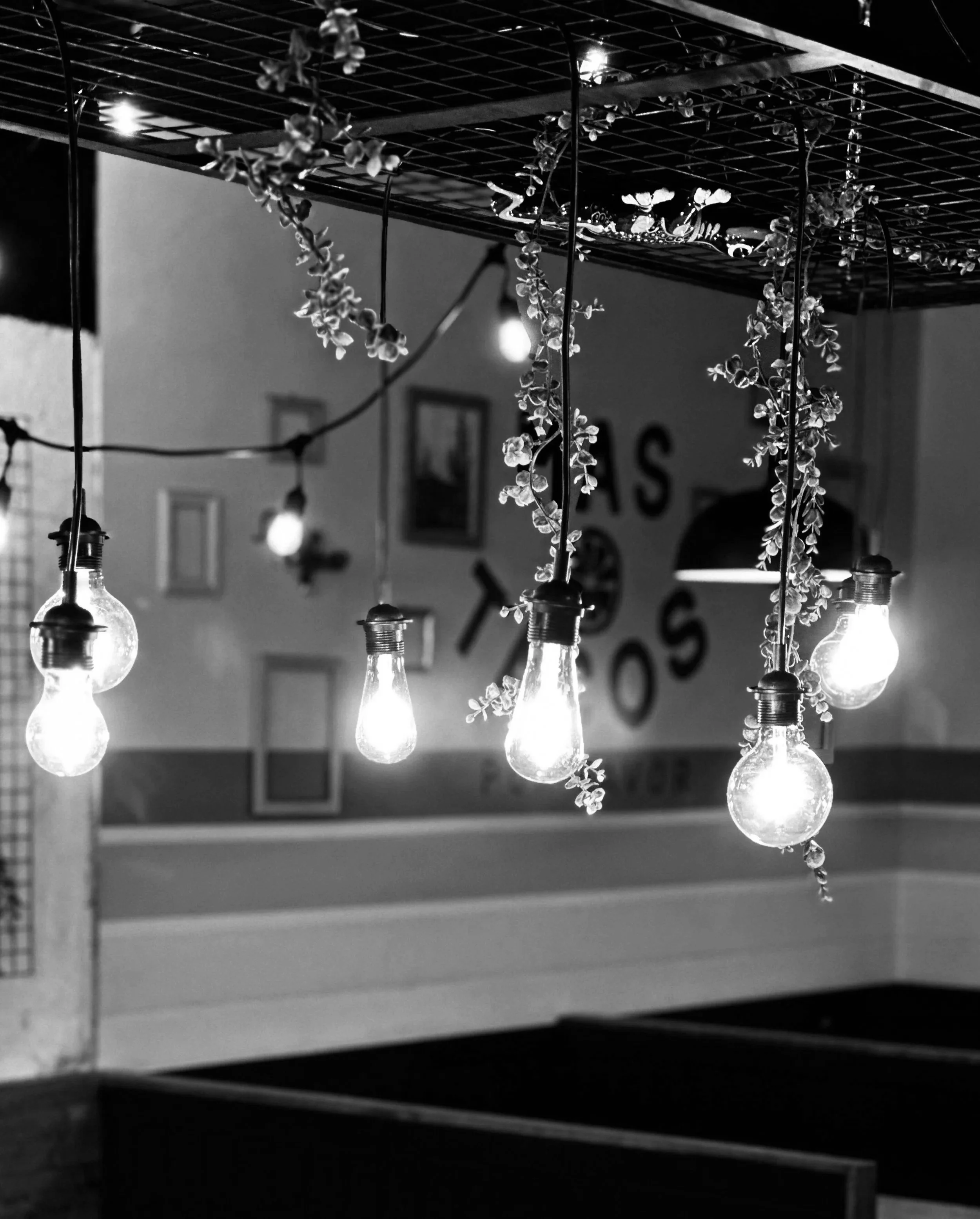 Hanging light bulbs and flower garland in a dimly lit room with framed pictures on the wall.