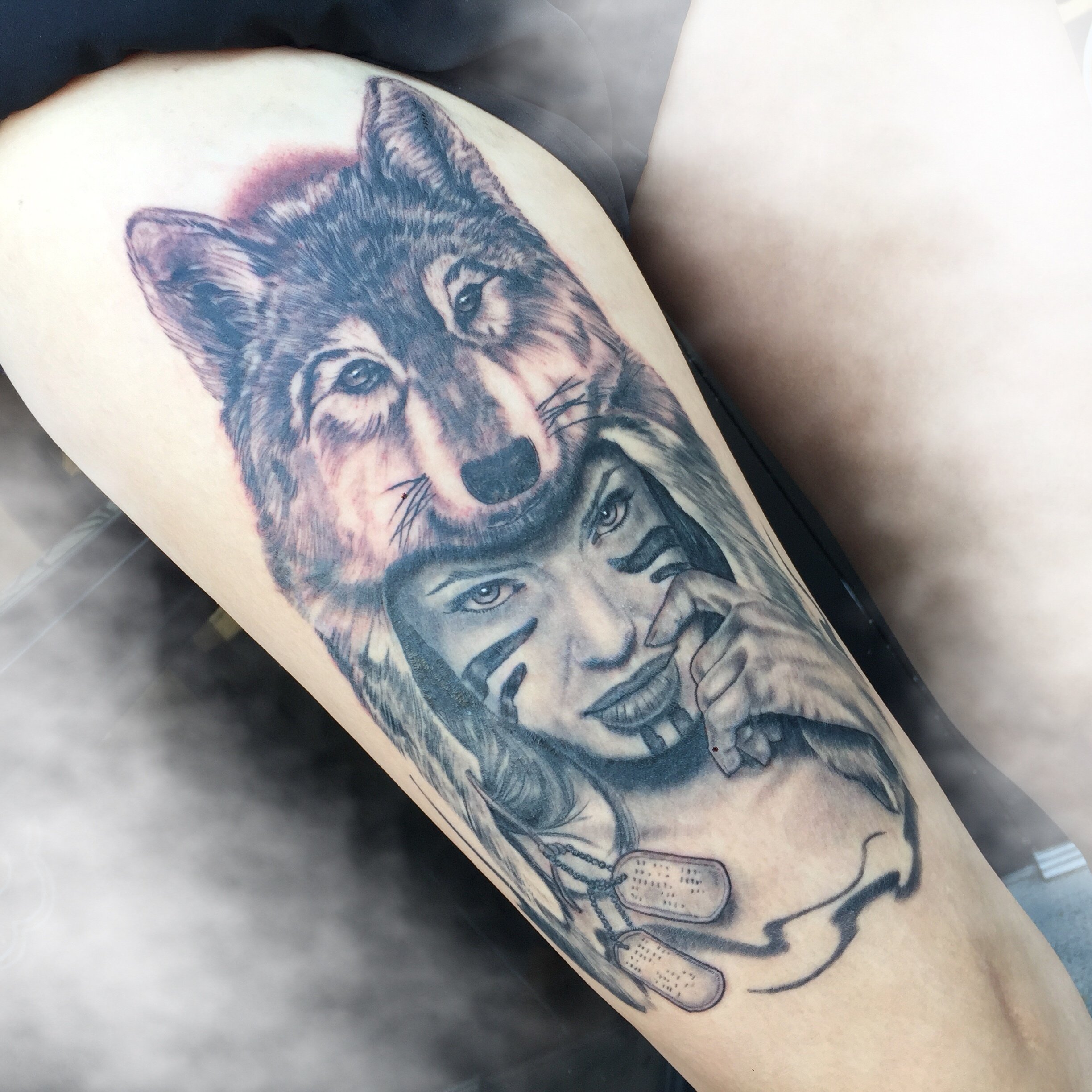 Black and grey tattoo of a woman's face and a wolf on a thigh. Tattoo done by Daniel Stewart at Signature Rose Professional Tattooing in Muncie Indiana.