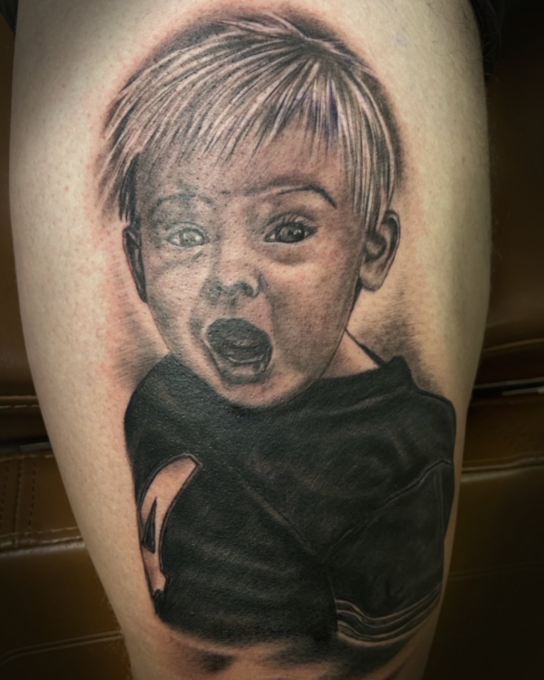 Black and grey realism portrait of a child in a football jersey. Thigh tattoo by Daniel Stewart at Signature Rose Professional Tattooing in Muncie Indiana.
