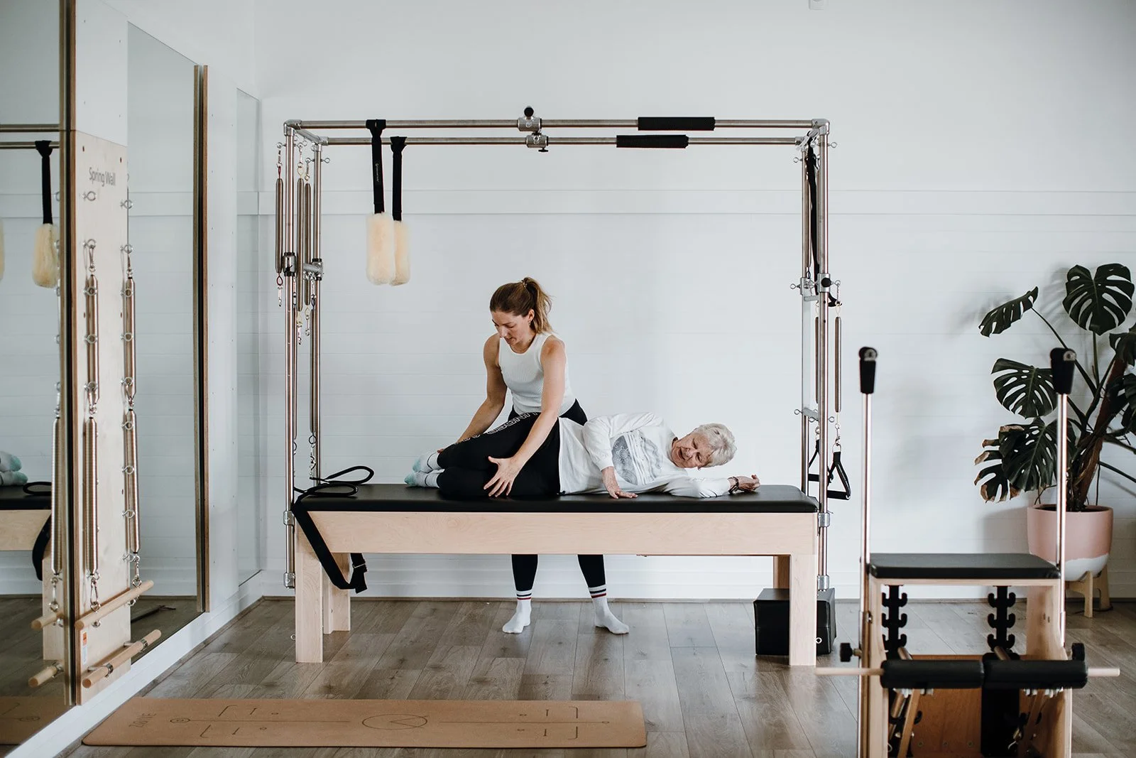 A women in a Clinical Pilates session lying sideways on a pilates trapeze table. She is being assisted by qualified Osteopathy instructor