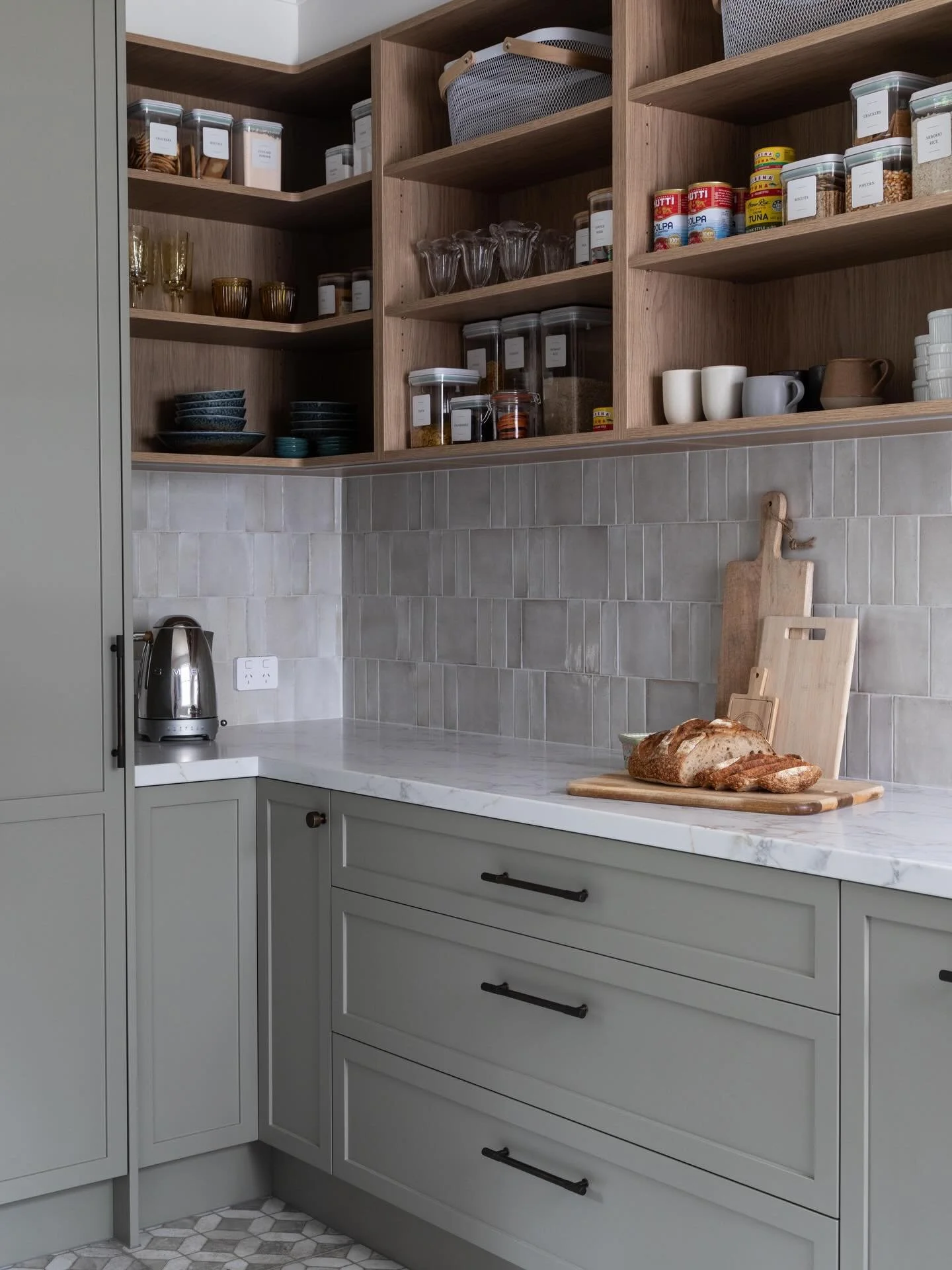 A layered mix of colour and texture allows this butler&rsquo;s pantry to sit seamlessly alongside the kitchen. Timber shelving adds warmth against the soft cabinetry, while the tiled splashback brings subtle depth and variation.
Designed for everyday
