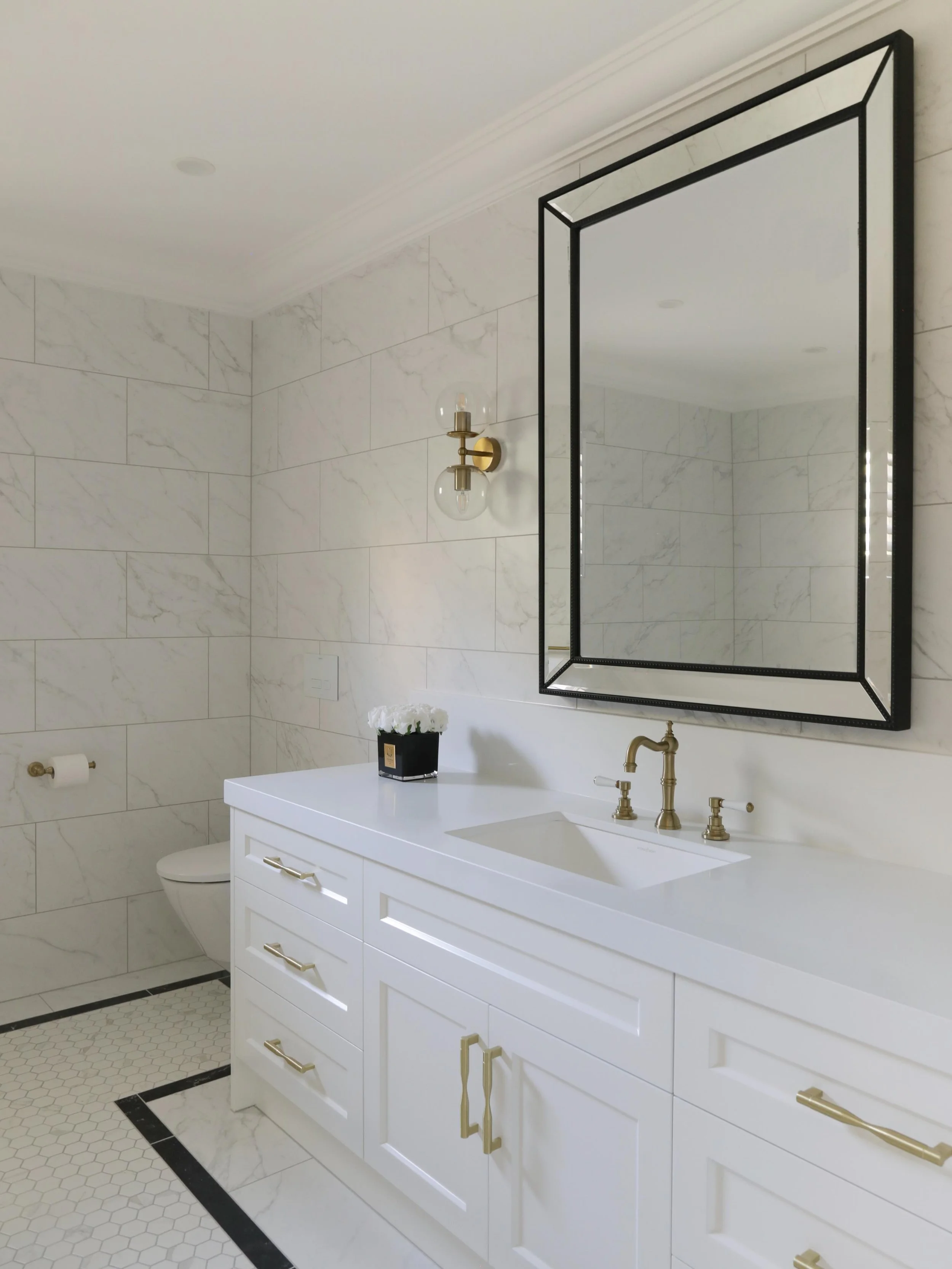 A timeless palette, thoughtful detailing, and a sense of quiet luxury.
This bathroom renovation pairs classic shaker joinery with soft marble-look tiling, warm brass fixtures, and contrasting black accents to create a space that feels both elegant an