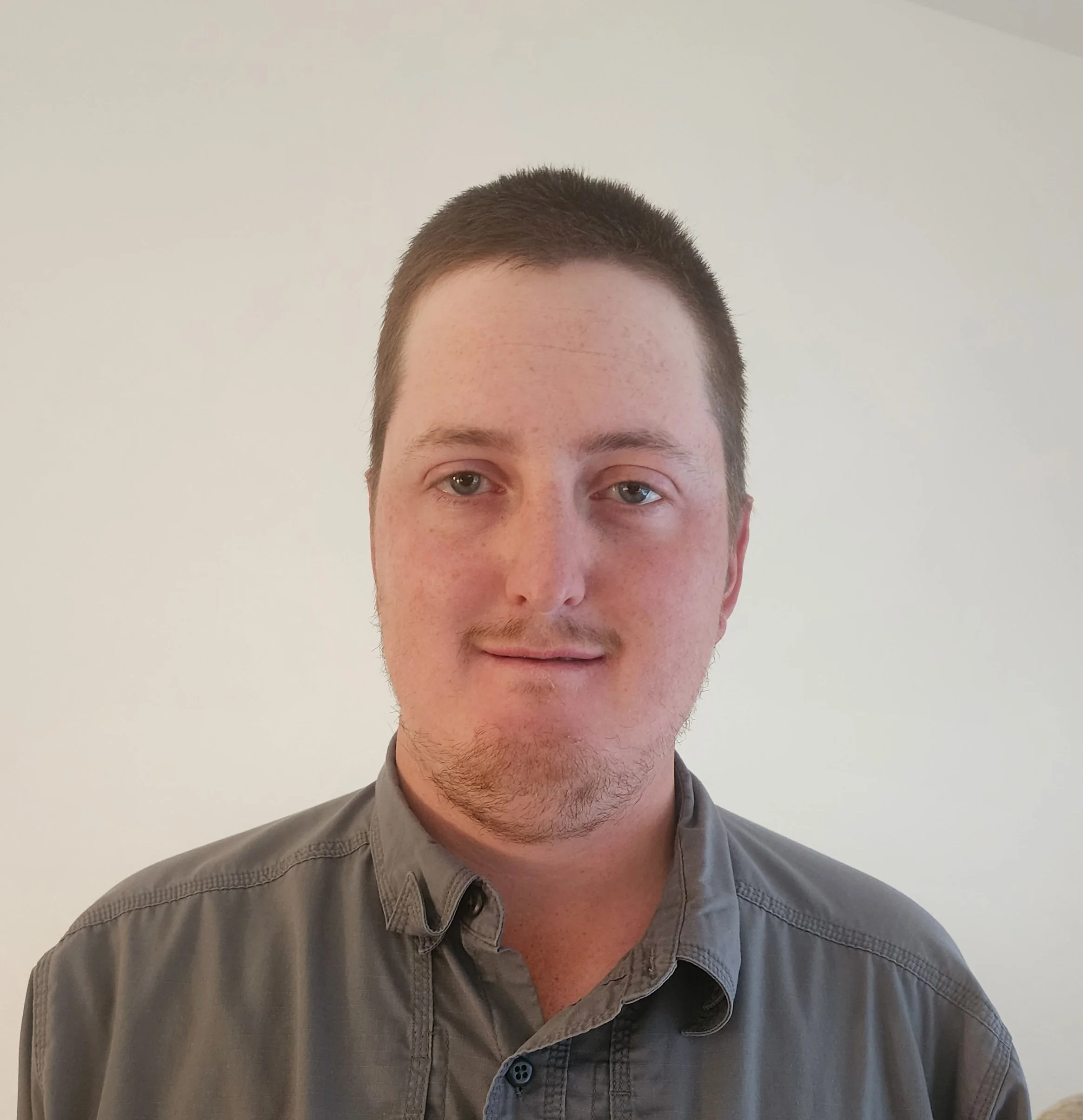 A person wearing a gray button-up shirt in front of a plain background.