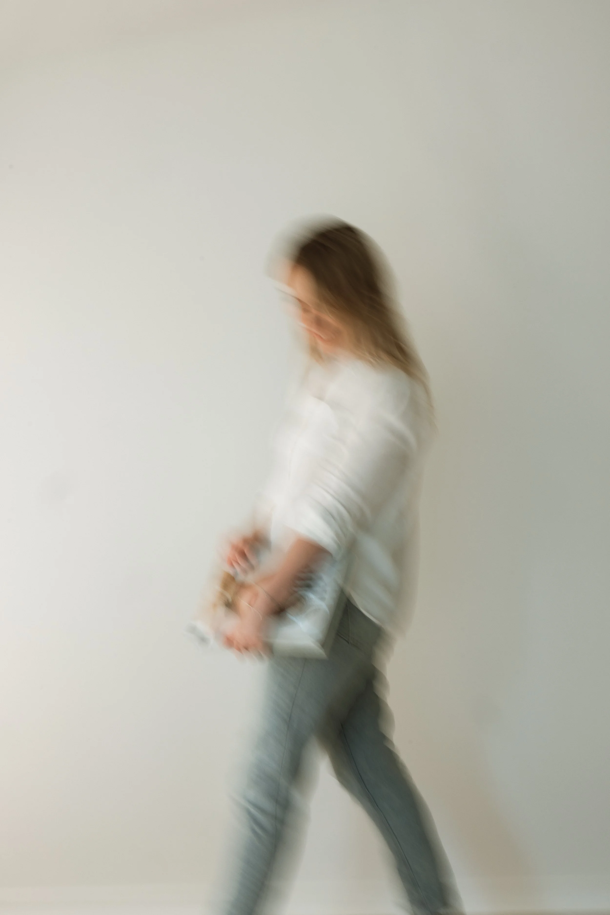 Blurred image of a person walking with a notebook in hand against a plain white wall.