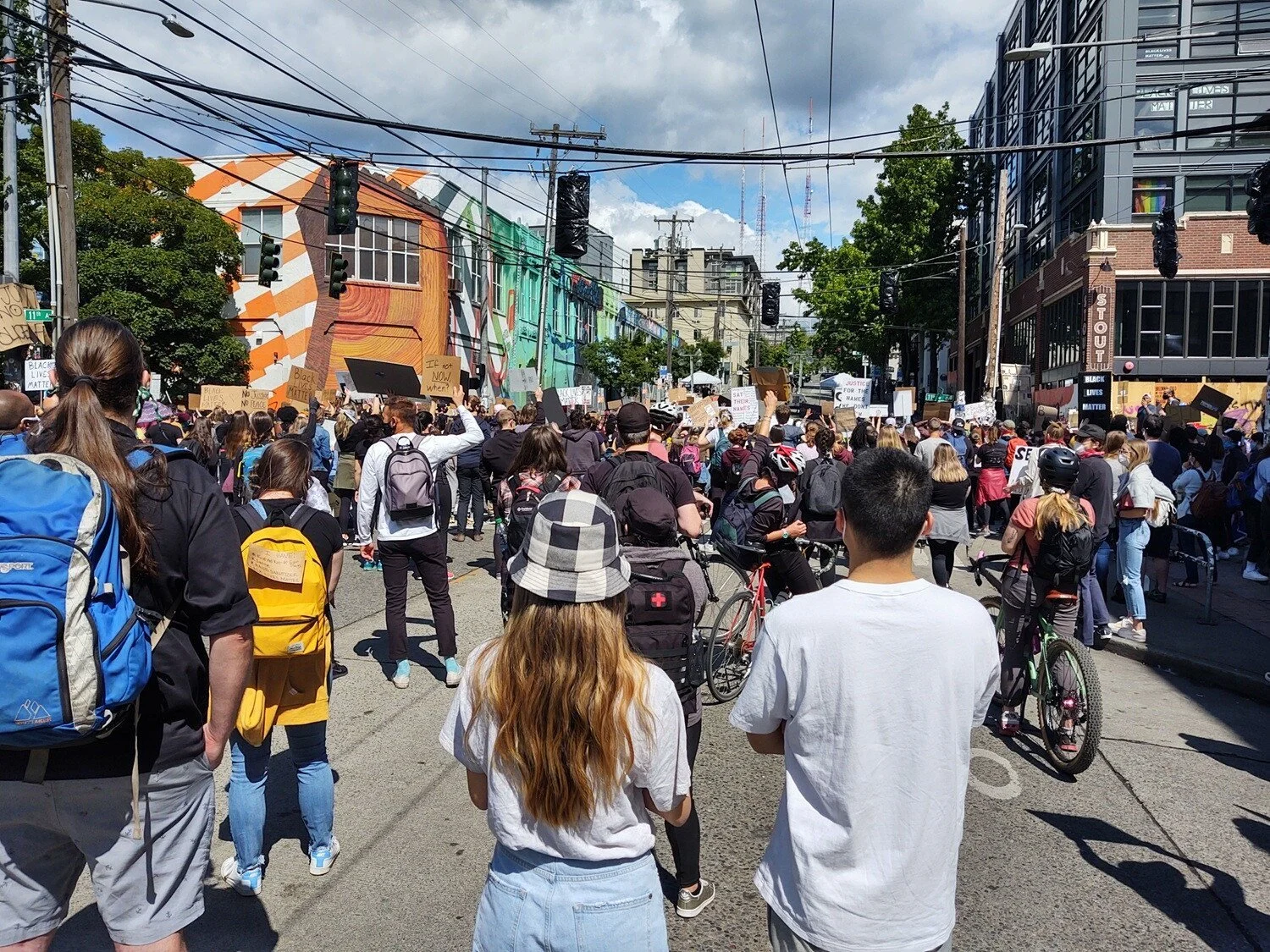 Protesters at 11th and Pine with bikes, helmets, backpacks, and signs. It is daylight and large clouds gather overhead.