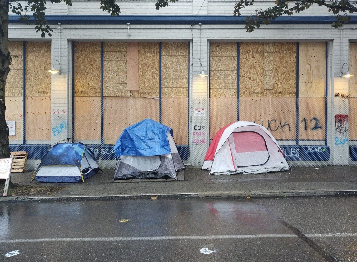 Three tents sit on the sidewalk in front of boarded-up windows. “Cop Free Zone” and “F--- 12” are written on the walls.