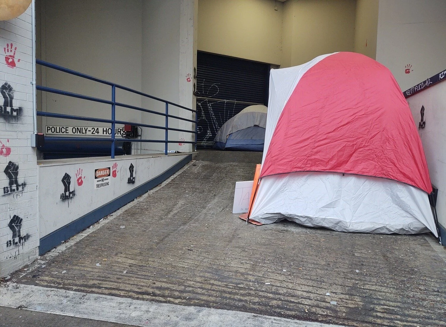 Two tents sit on a ramp outside the precinct. The brick walls are covered in stencils of black fists and red hand prints.