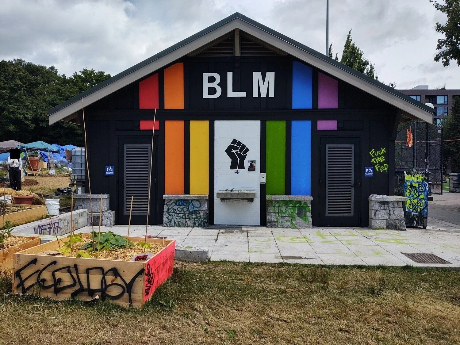 A black building with vertical stripes the color of the Pride flag. “BLM” and a fist are incorporated into the design.