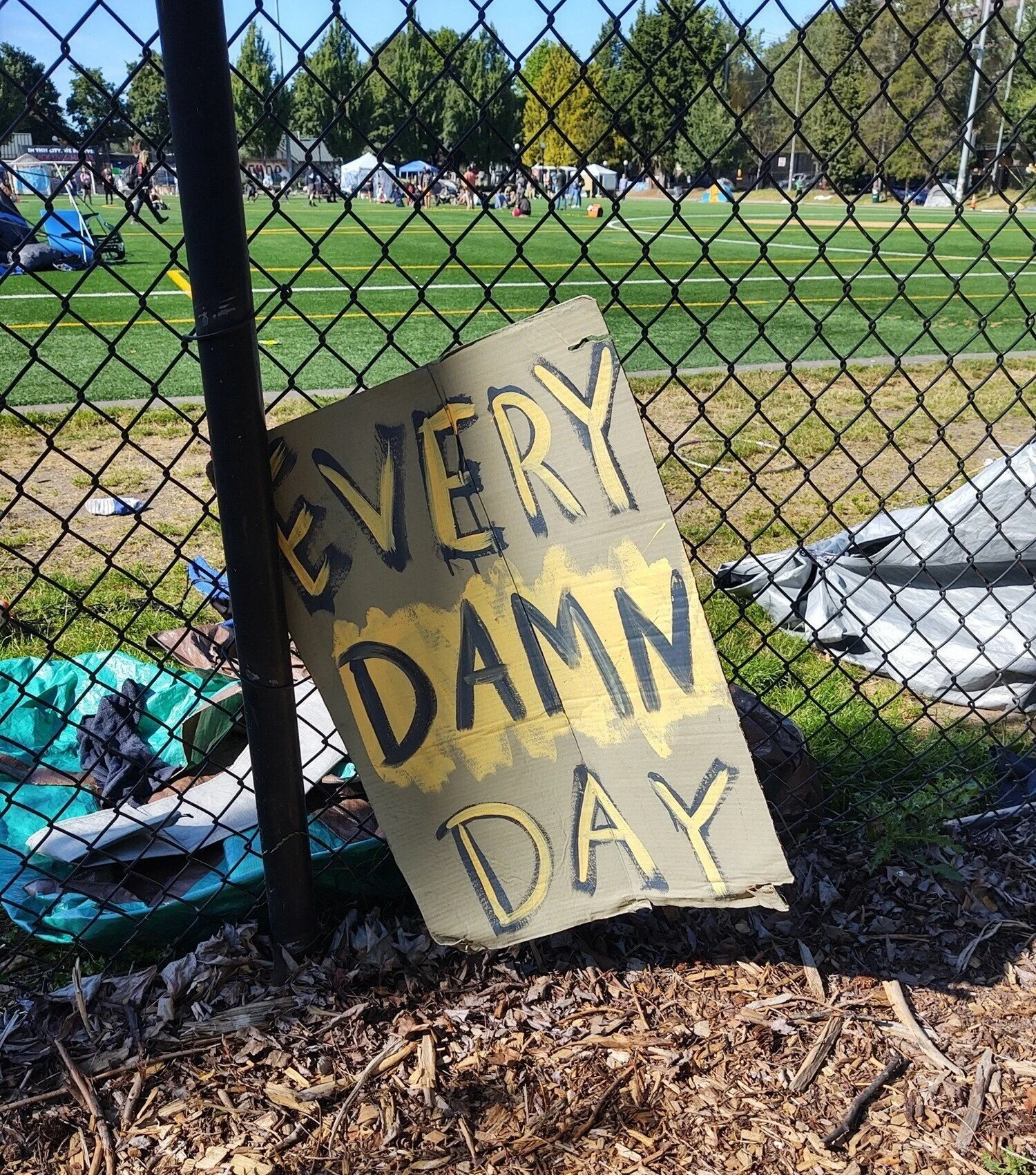 Cardboard sign reads “every d--n day” in yellow and black lettering.