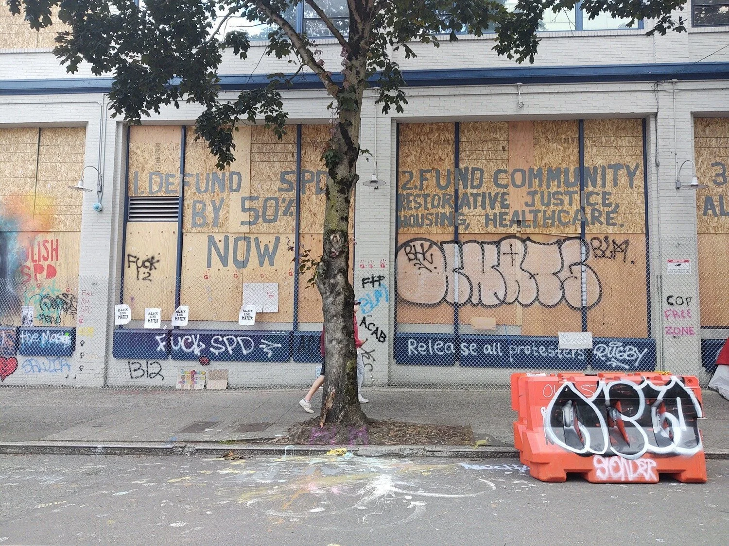 Large lettering reads, “1. Defund SPD by 50% now. 2. Fund community restorative justice, housing, healthcare.”