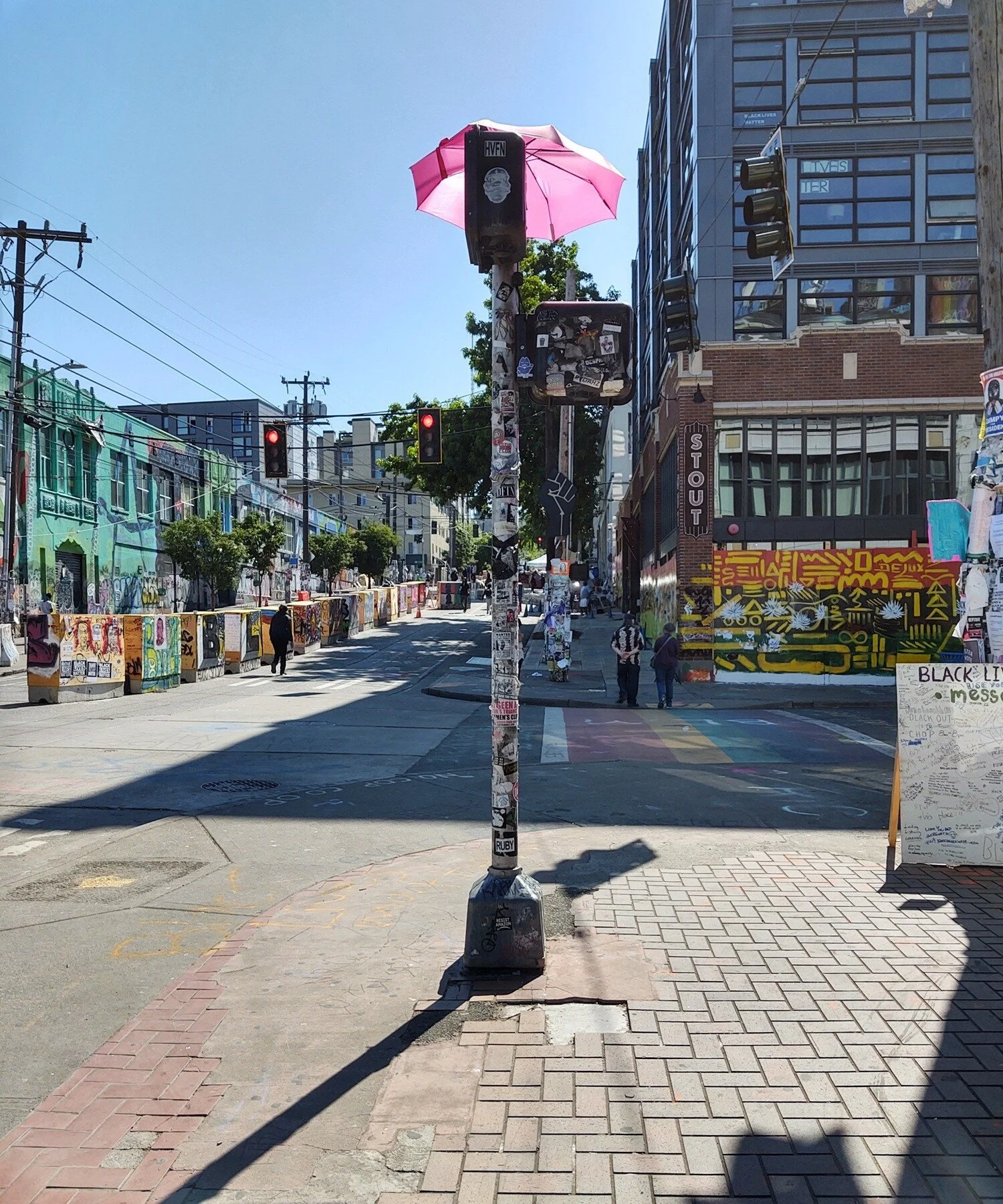 An open pink umbrella rests atop a street crossing sign. About 12 people are visible from a vantage point at 11th and Pine.
