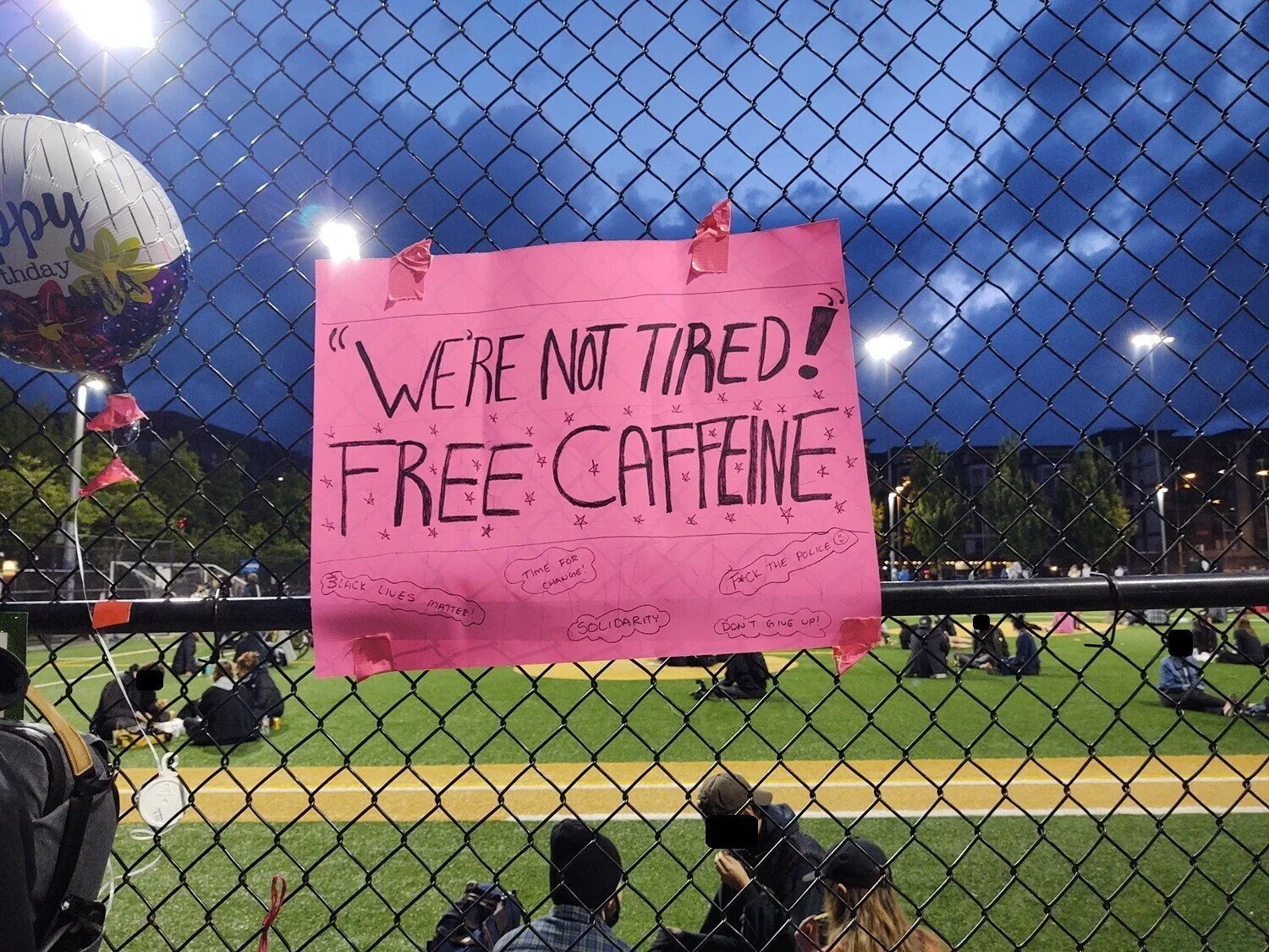"We’re Not Tired! Free Caffeine" reads a pink sign attached to the fence at Cal Anderson Park.