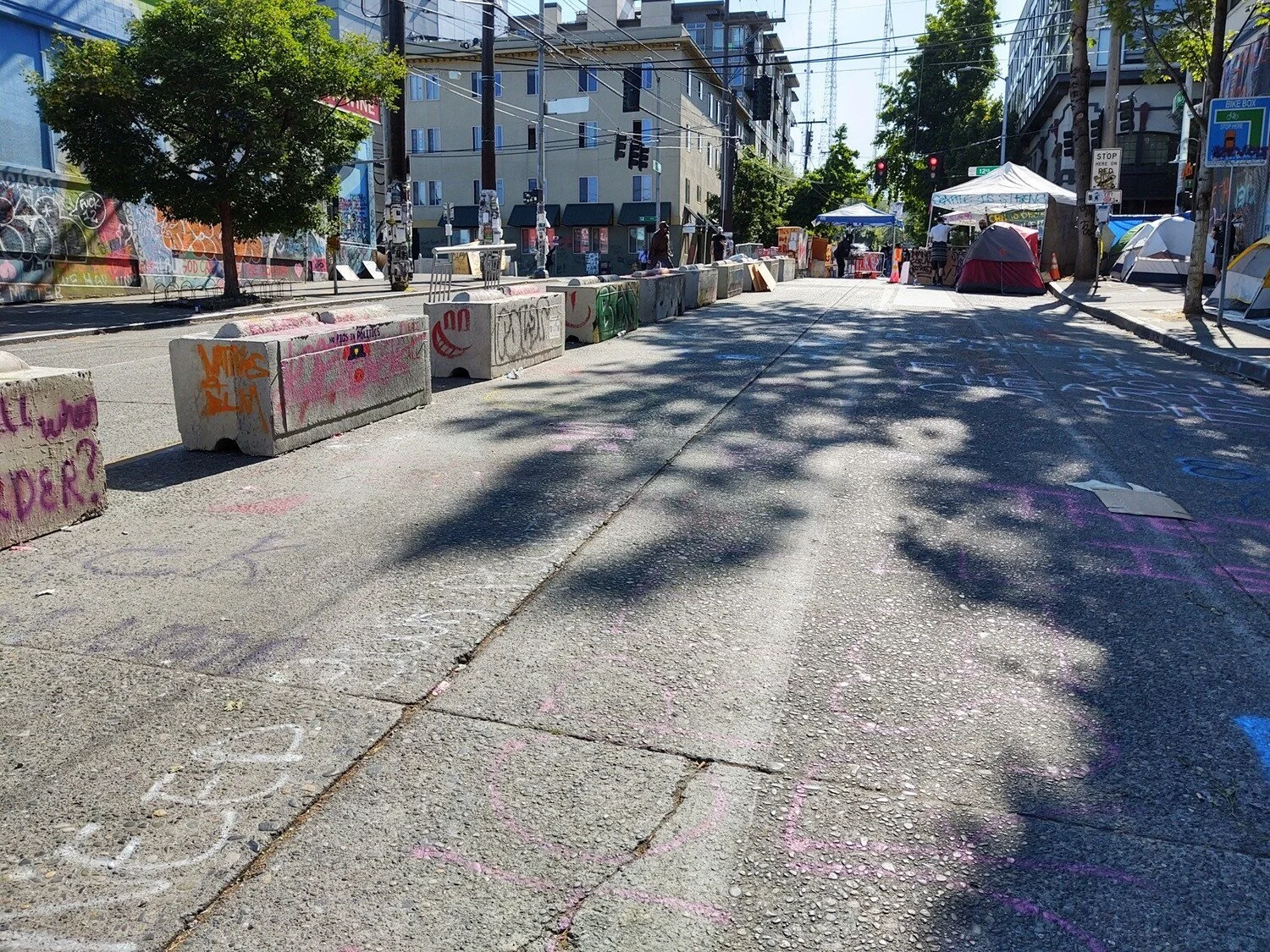 Concrete barricades in the middle of Pine St. Tents on the sidewalk. A few people are under event tents in the intersection.