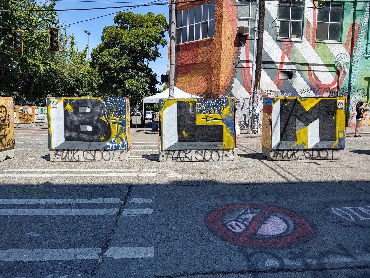 Three barricades each display one letter of “BLM”. “F--- SDOT” is spray pained on the bottom of each.”