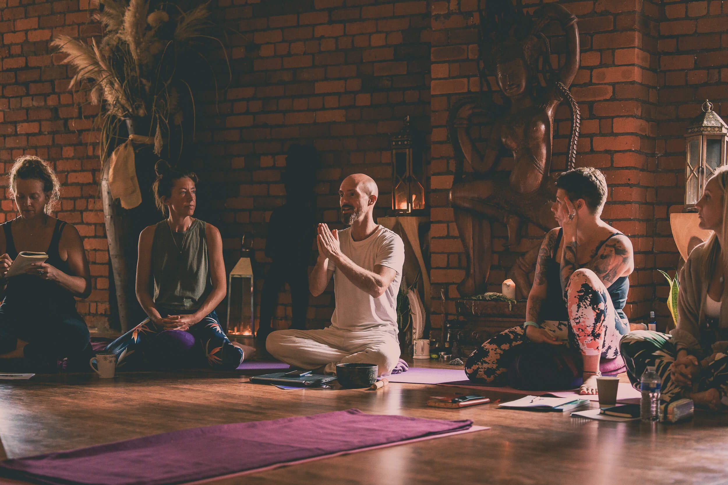 Group of people taking part in a yoga and wellbeing workshop in a brick studio, seated on yoga mats around the instructor.
