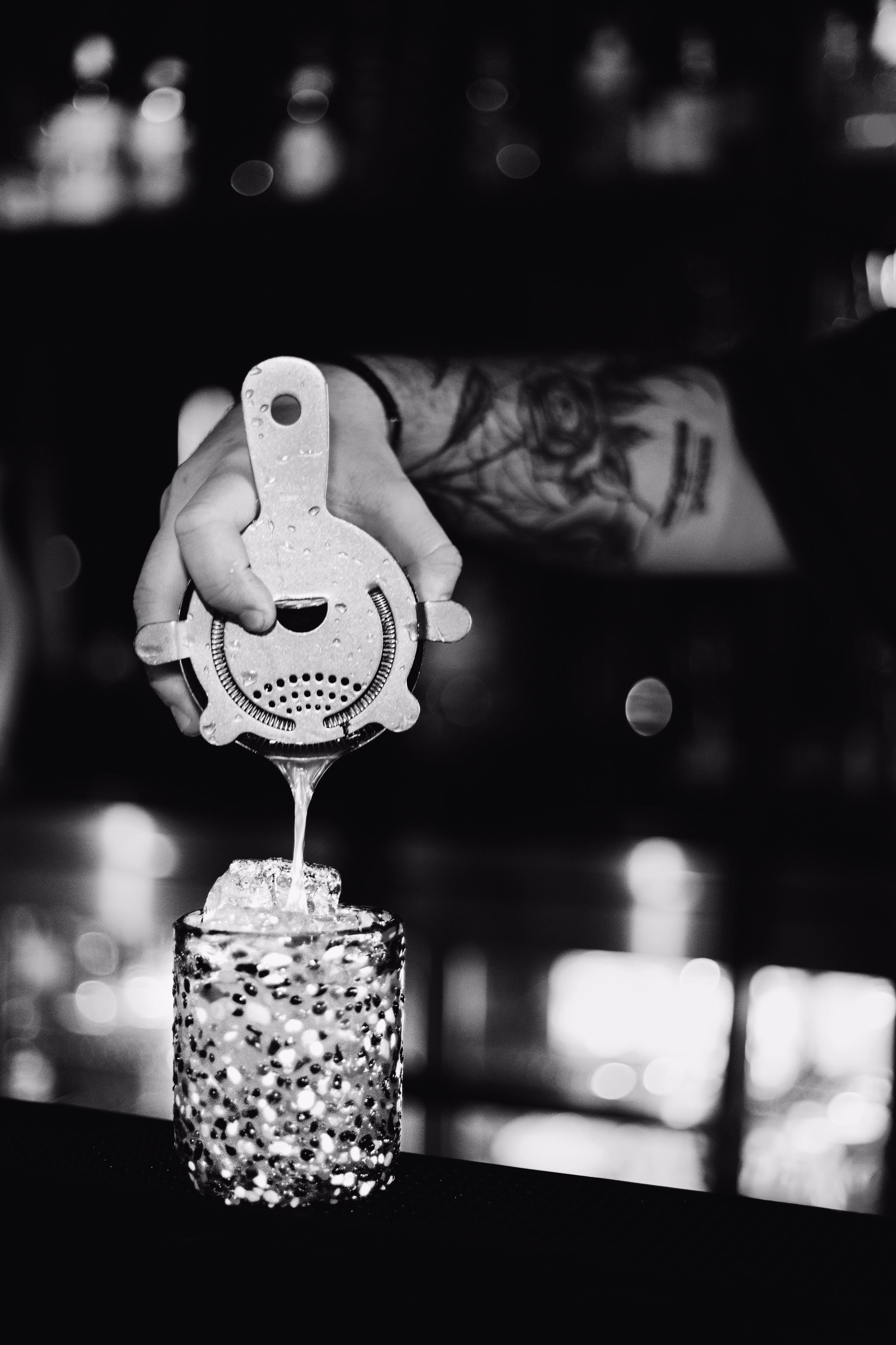 A skilled Silk Utica bartender straining and pouring a handcrafted cocktail into a glass, showcasing the expert craft cocktail experience at Utica New York's premier cocktail and dessert bar.