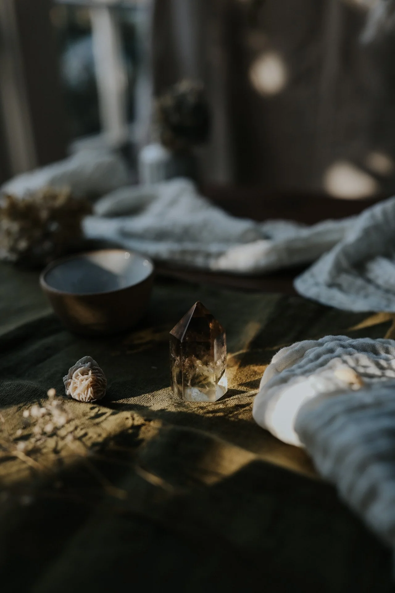Clear quartz crystal on a table with a ceramic bowl and cloth.