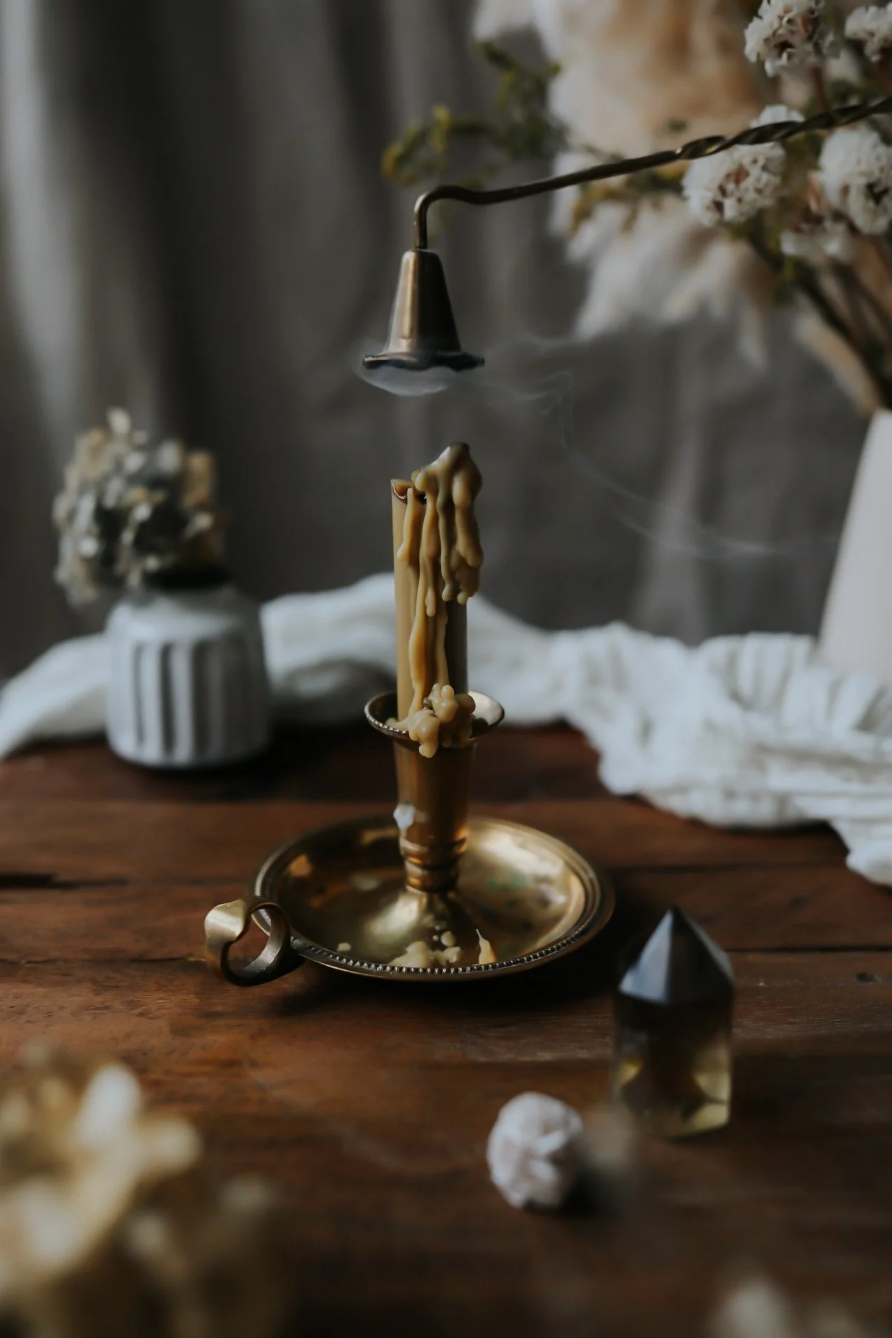Vintage melting candle holder with snuffer, smoke, and decorative items on wooden table.