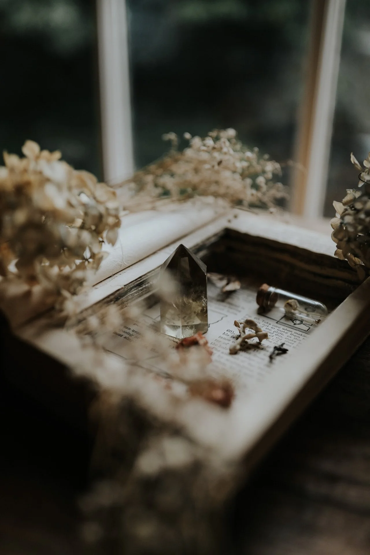 Vintage book with crystal, dried flowers, and small glass vial on a wooden table.