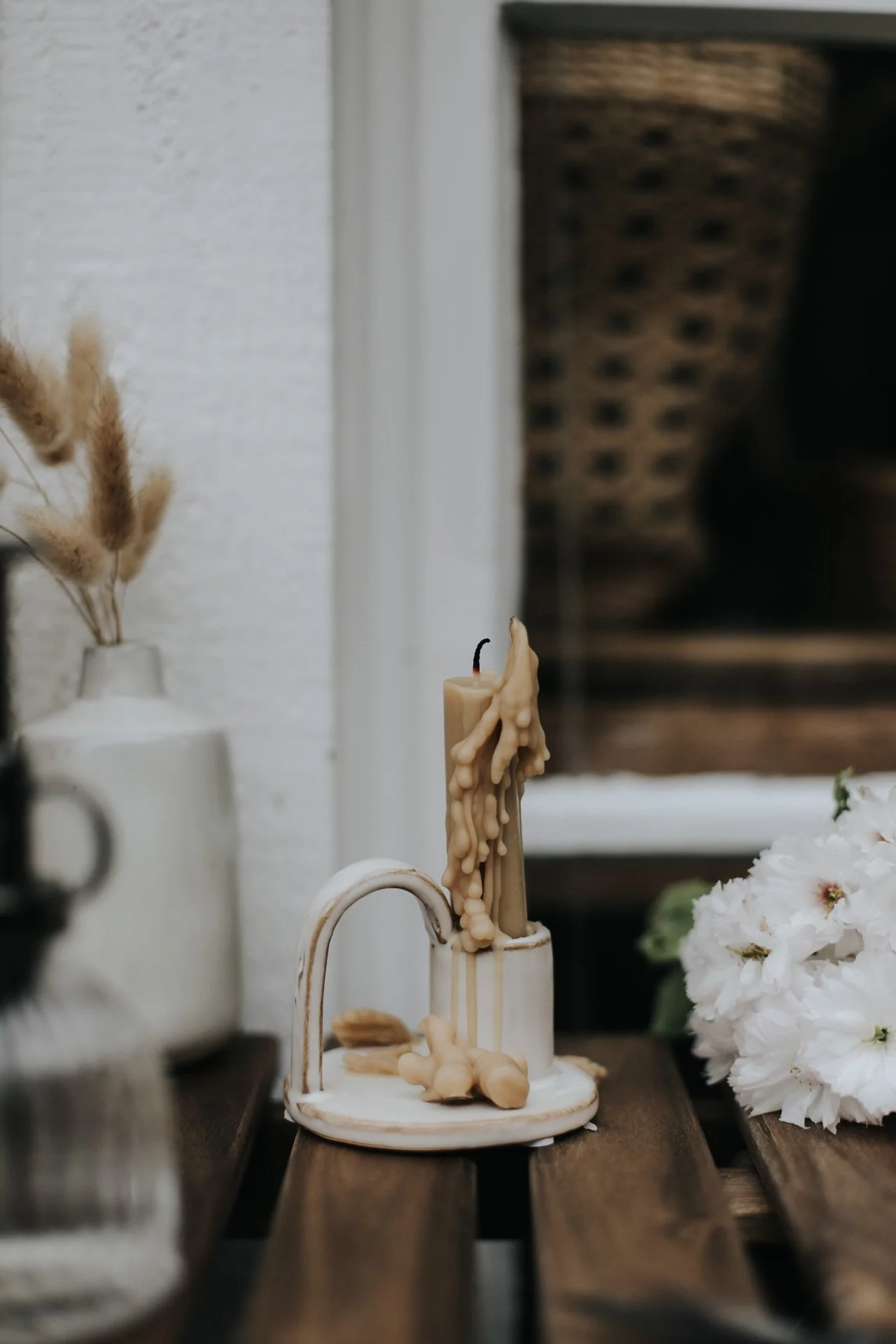 Melted candle on wooden table with vase and white flowers